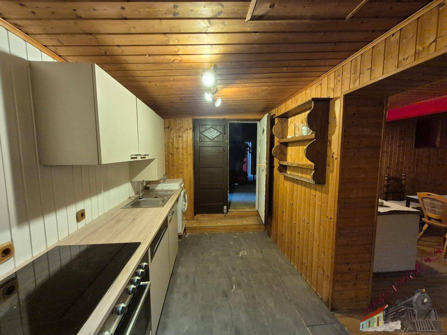 Einfache Küche mit Holzvertäfelung, weißen Oberschränken und einem Kochfeld mit Backofen.