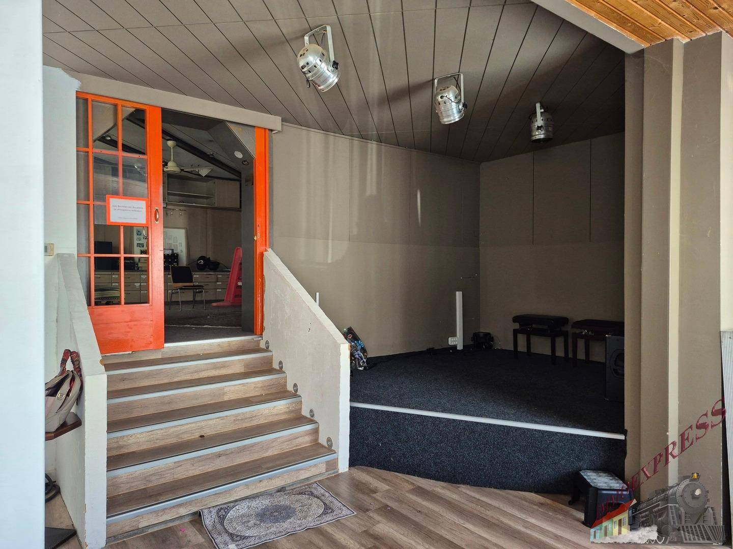 Eingangsbereich mit Treppe, Holzboden und einer orangefarbenen Tür zu einem weiteren Raum.