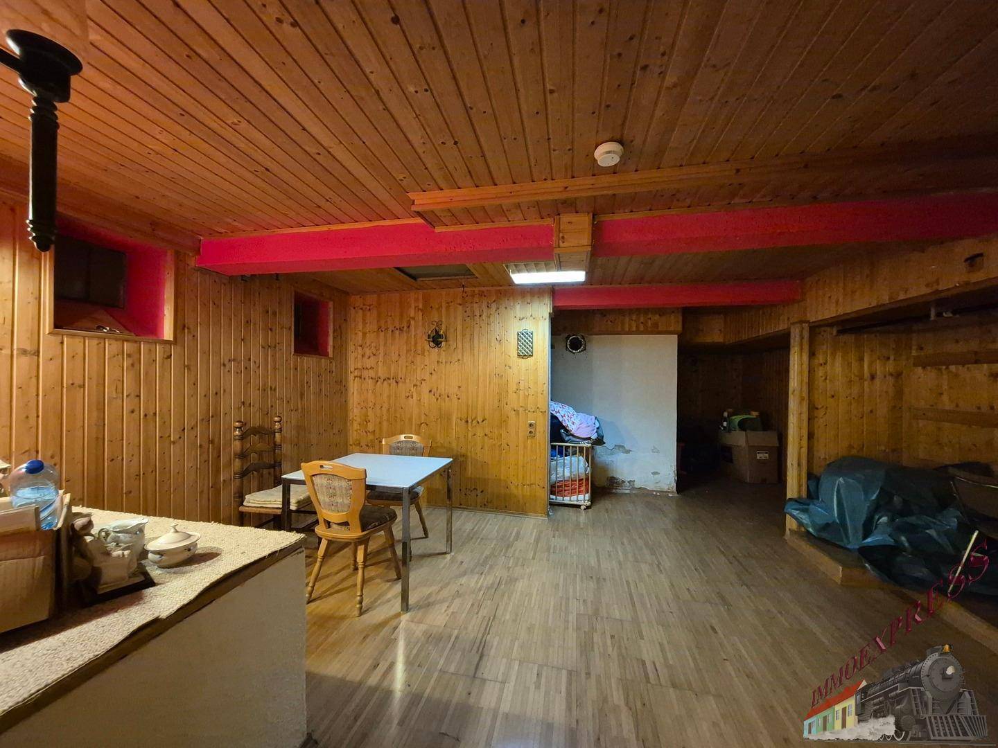 Rustikaler Wohnbereich mit Holzwänden, Holzdecke und einem Esstisch in der Mitte des Raumes.