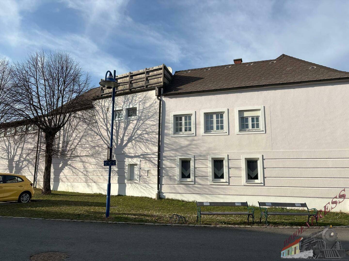 Seitenansicht des Gebäudes mit Bäumen, Bänken und einer hohen Mauer im Hintergrund.