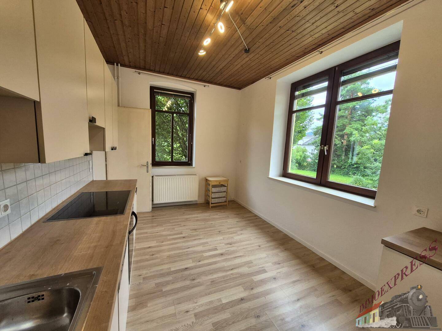 Funktionale Küche mit Holzdecke, Laminatboden und Blick ins Grüne durch das Fenster.