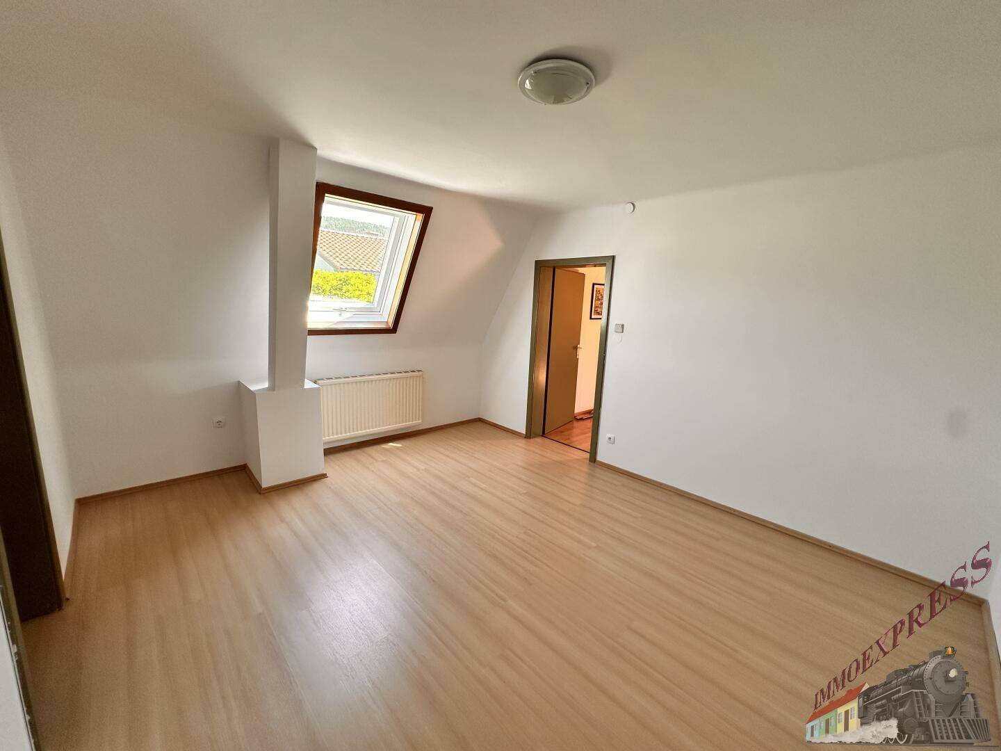 Geräumiges Dachzimmer mit Laminatboden, Dachfenster und weiß gestrichenen Wänden.