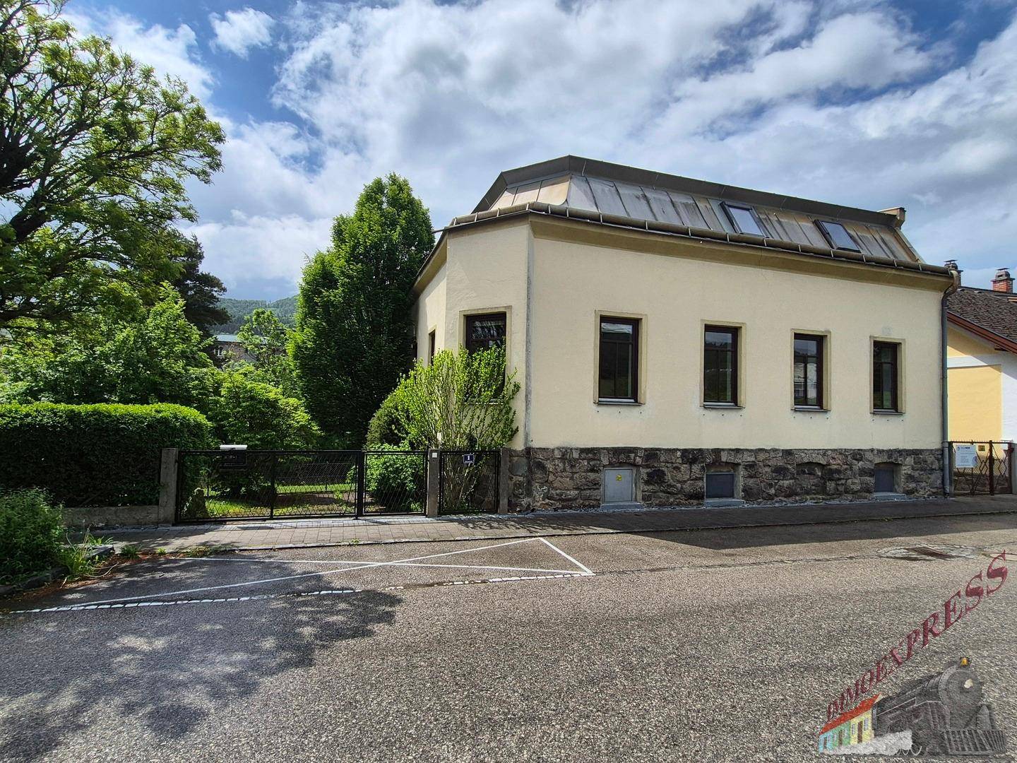 Ansicht des Hauses von der Straße mit gepflegtem Vorgarten und Zaun unter bewölktem Himmel.