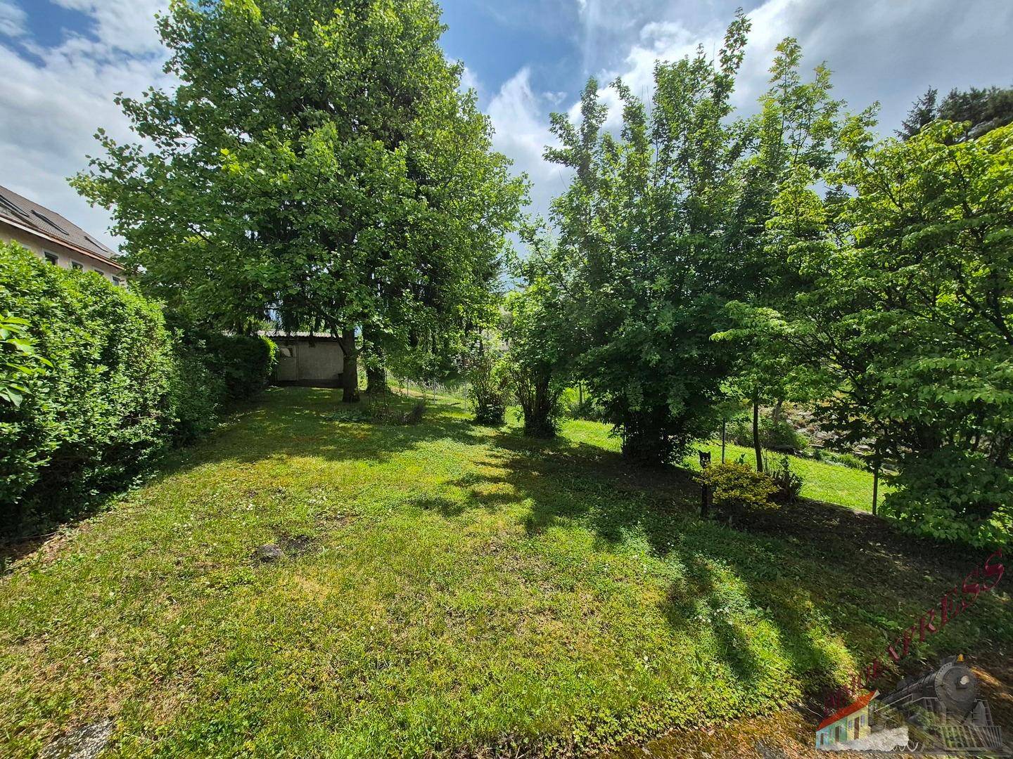 Weitläufiger Garten mit Rasenfläche und verschiedenen Bäumen unter blauem Himmel.