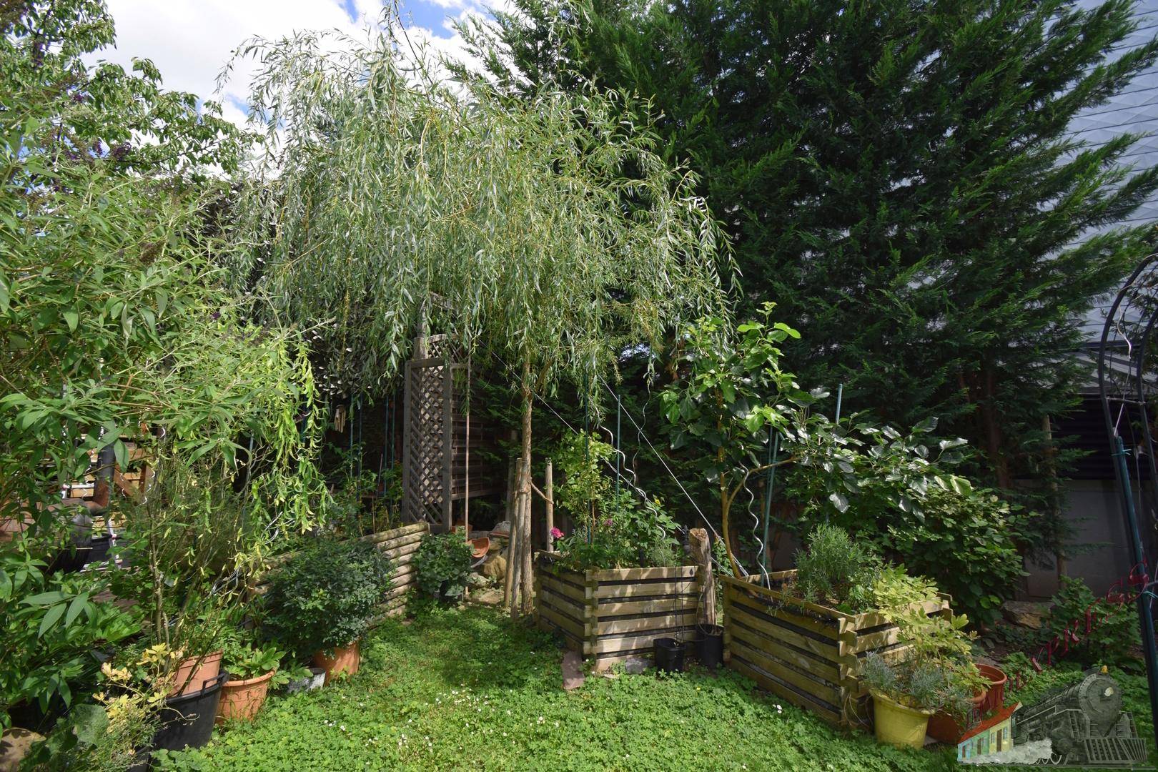 Üppiger Gartenbereich mit verschiedenen Pflanzen, Bäumen und Hochbeeten.