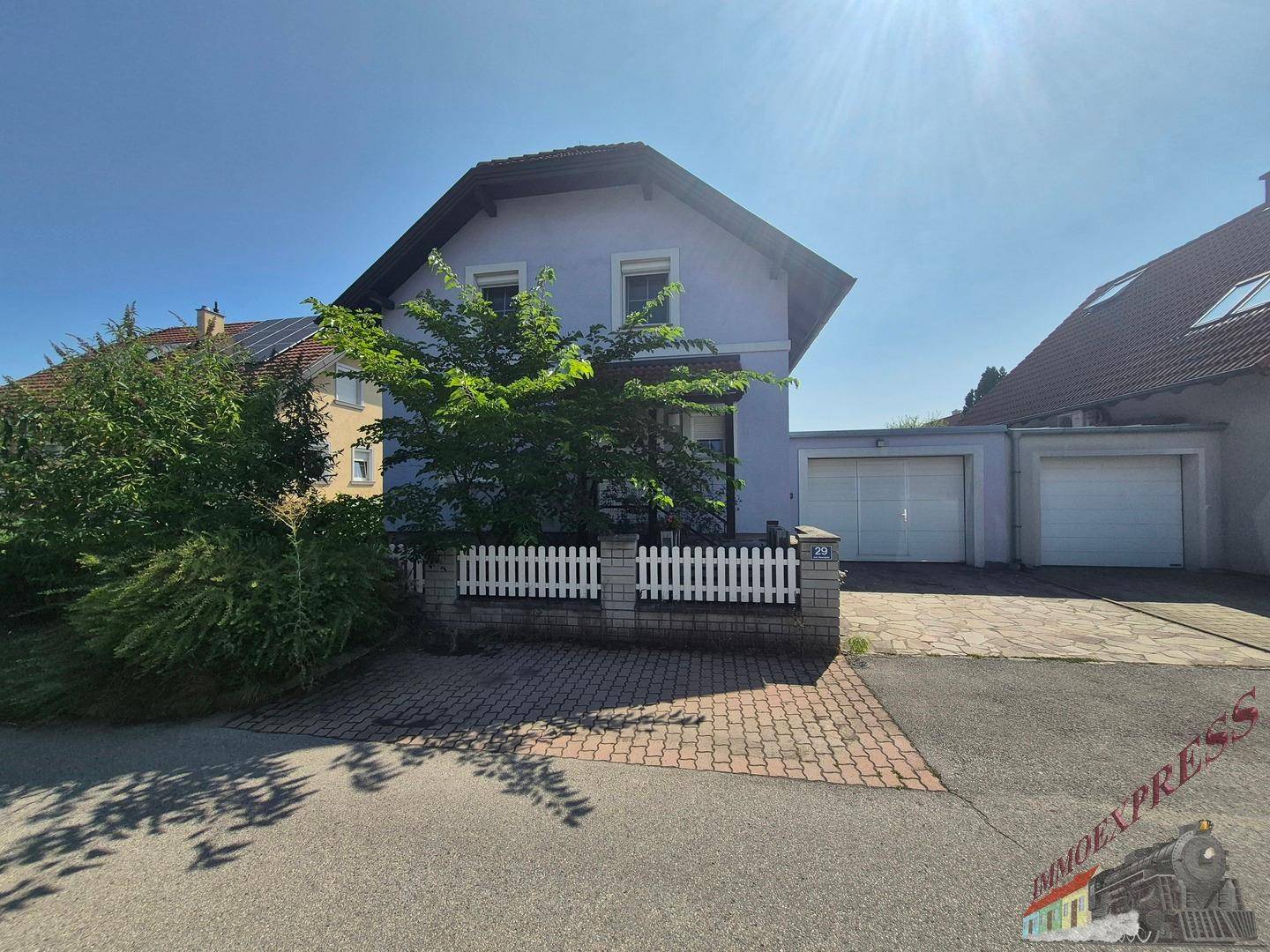 Vorderansicht des Hauses mit Garage, gepflasterter Einfahrt und einem kleinen Vorgarten mit Zaun.