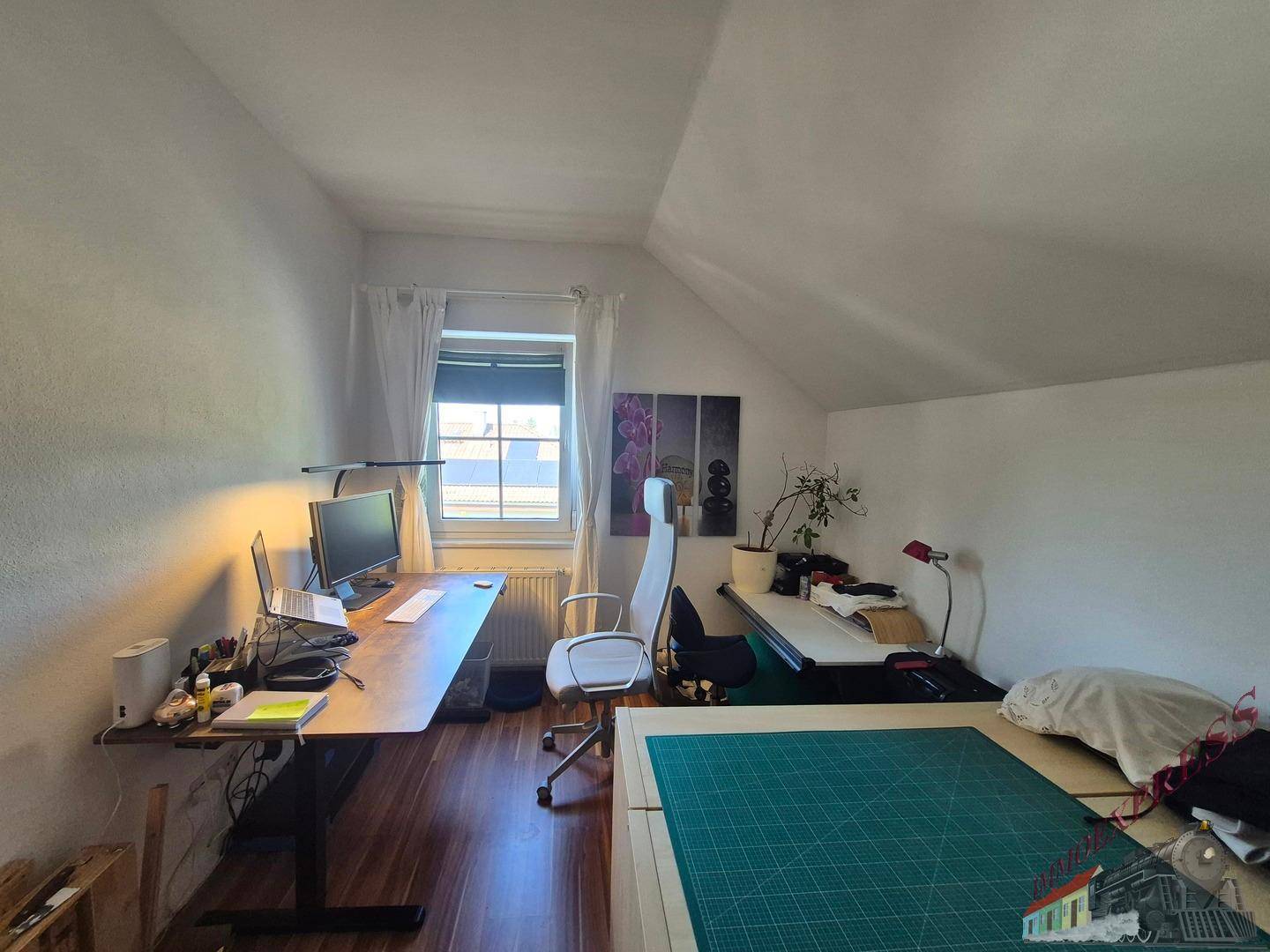 Helles Arbeitszimmer im Dachgeschoss mit Schreibtischen, Bürostuhl und Laminatboden.