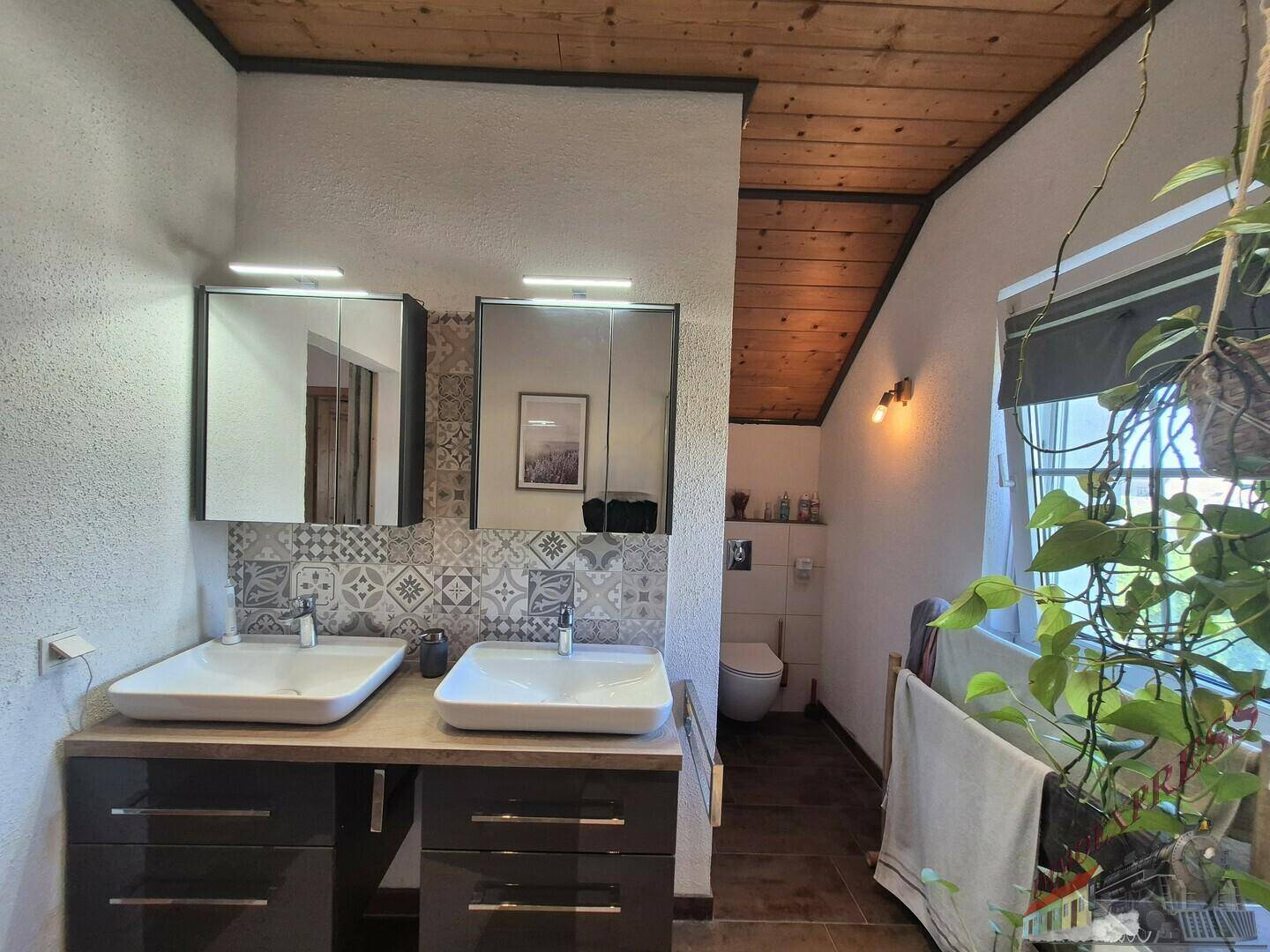 Badezimmer mit Doppelwaschbecken, Spiegelschränken und dekorativen Fliesen im Dachgeschoss.