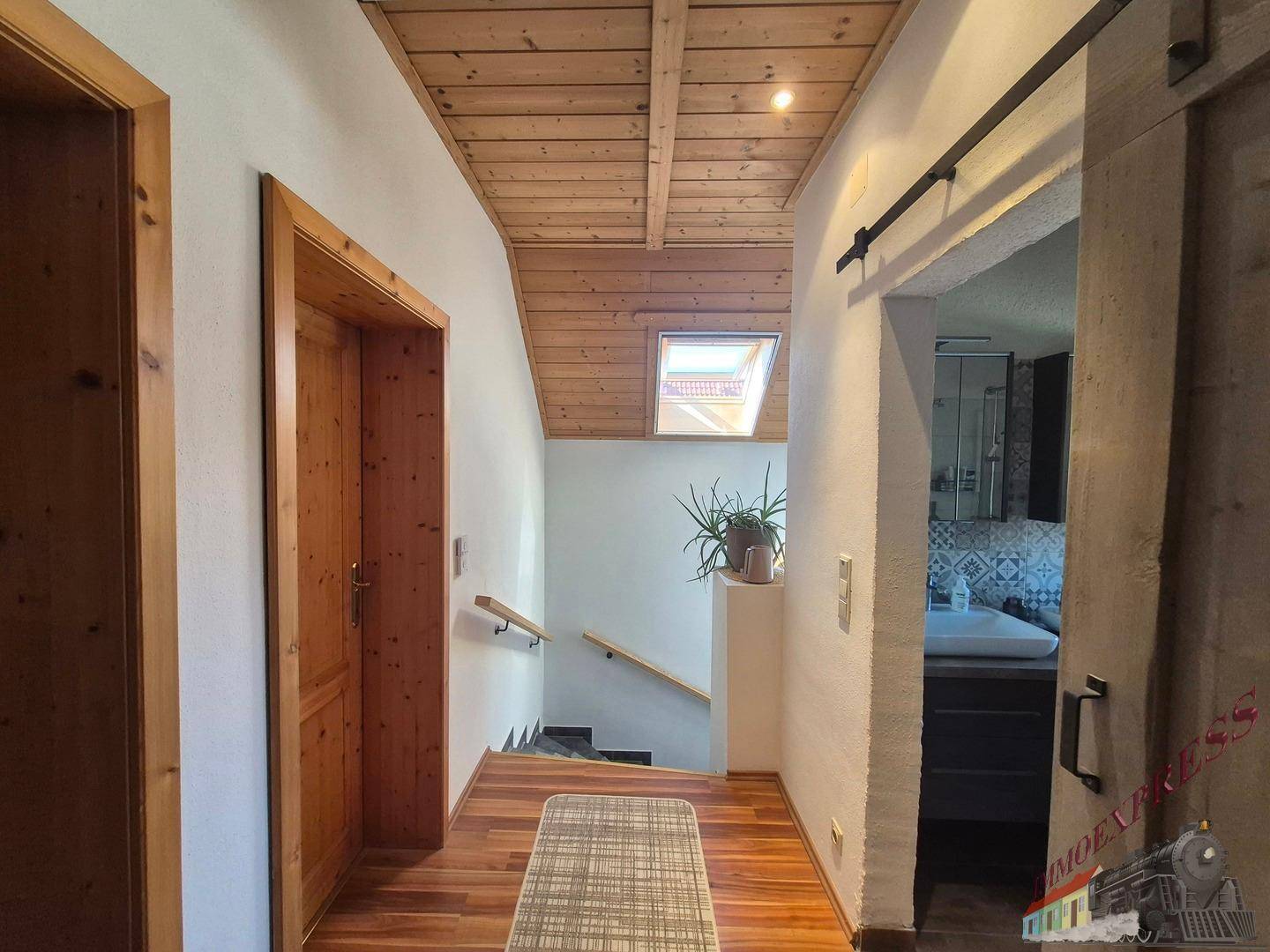Heller Flur mit Holzdecke, Holztreppe und Parkettboden, der zu weiteren Räumen führt.