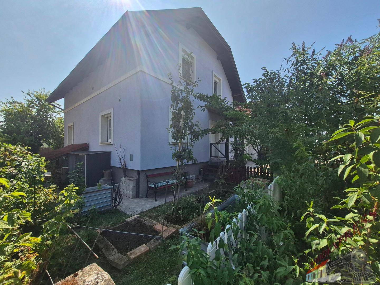 Seitenansicht des Hauses mit einem kleinen Gartenbereich, Hochbeeten und einem Holzzaun.