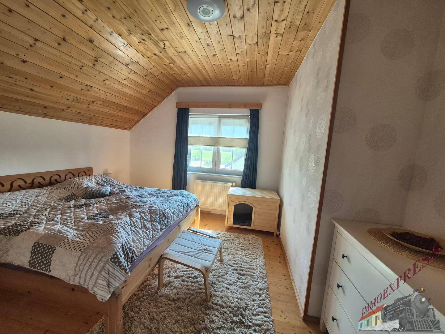 Gemütliches Schlafzimmer im Dachgeschoss mit Holzbett, Teppichboden und Holzdecke.