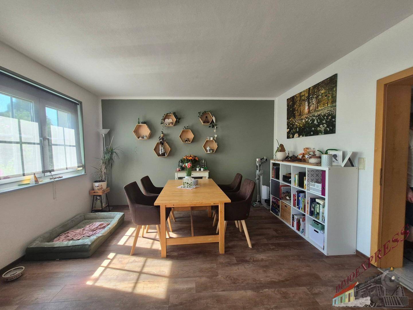 Essbereich im offenen Wohnraum mit Holztisch, Stühlen und dekorativen Wandregalen.