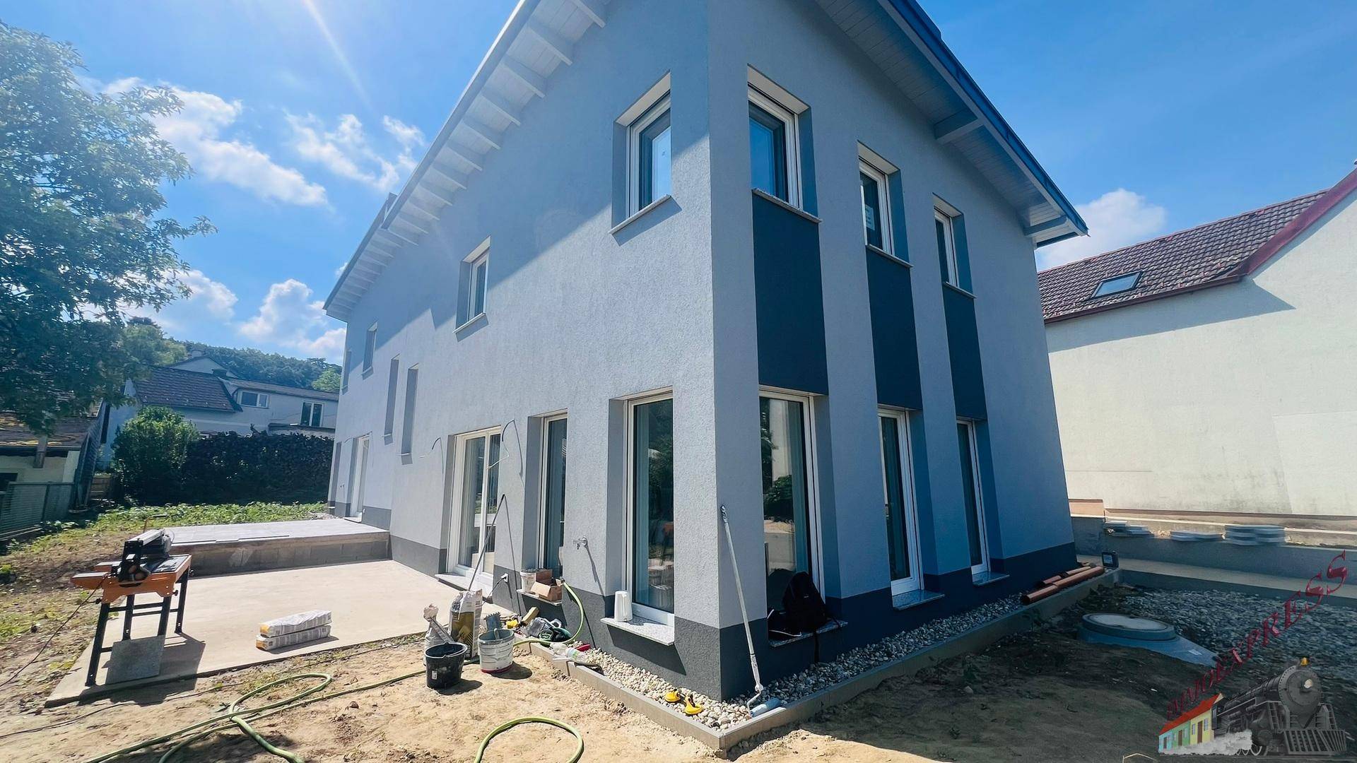 Neubau-Einfamilienhaus mit moderner Fassade, großen Fenstern und einer neuen Terrasse im Rohzustand.
