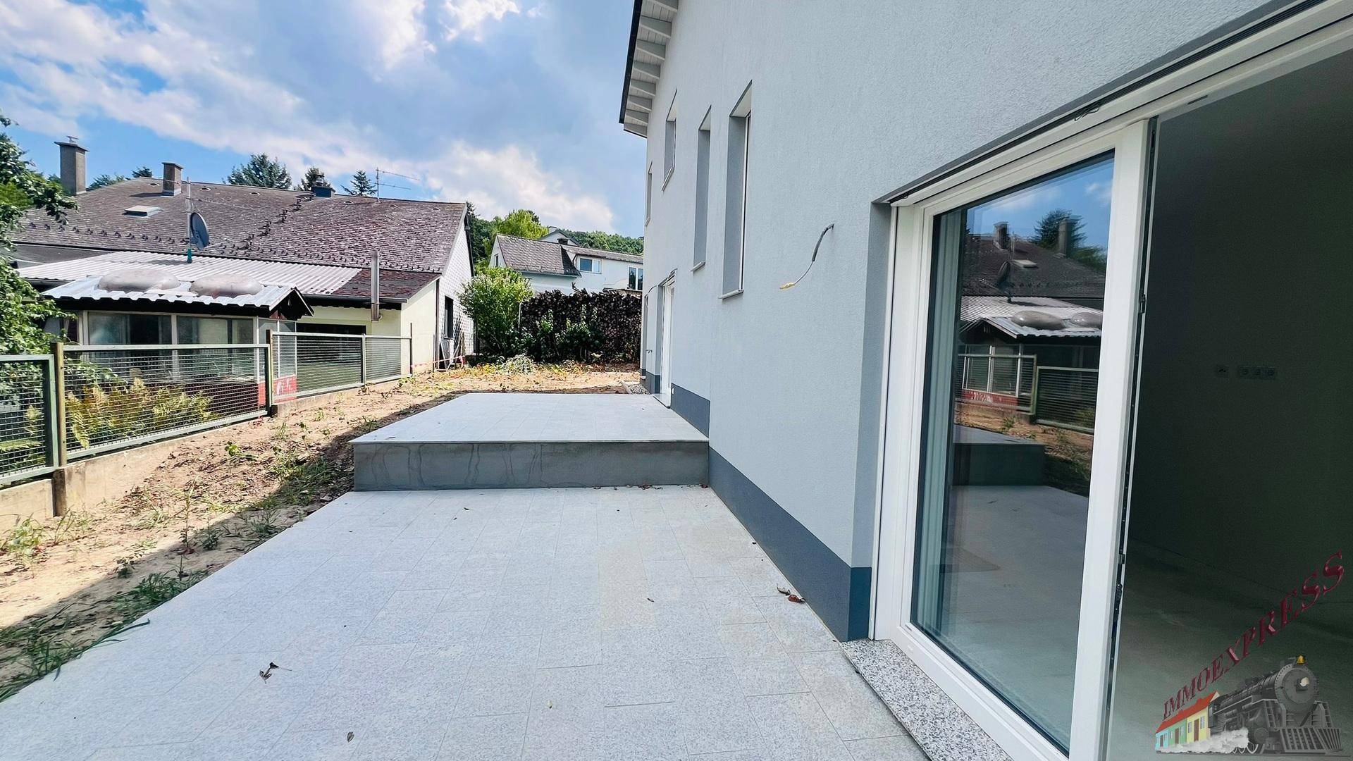 Großzügige, gepflasterte Terrasse am Neubau mit direktem Zugang zum Innenbereich durch Glasschiebetüren.