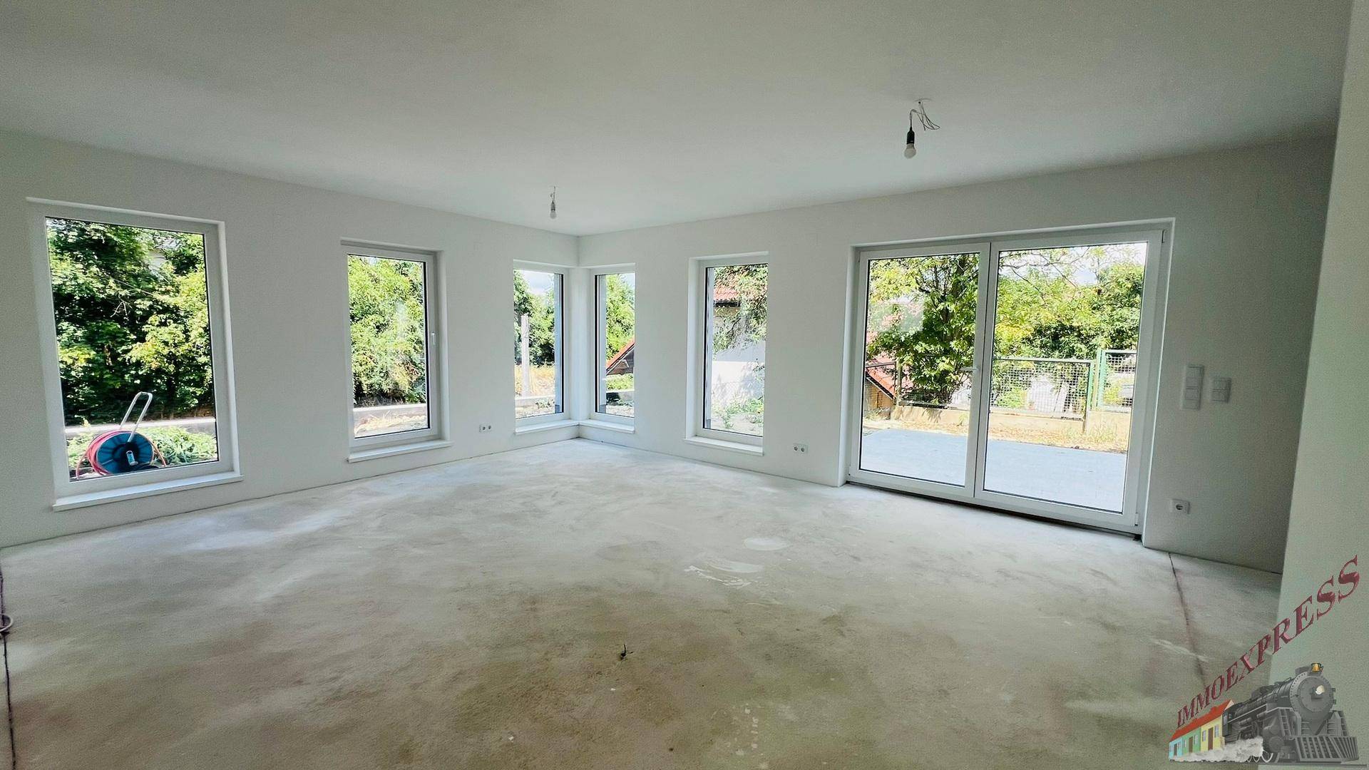 Heller, geräumiger Wohnbereich im Neubau mit vielen Fenstern und Blick ins Grüne, noch ohne Bodenbelag.
