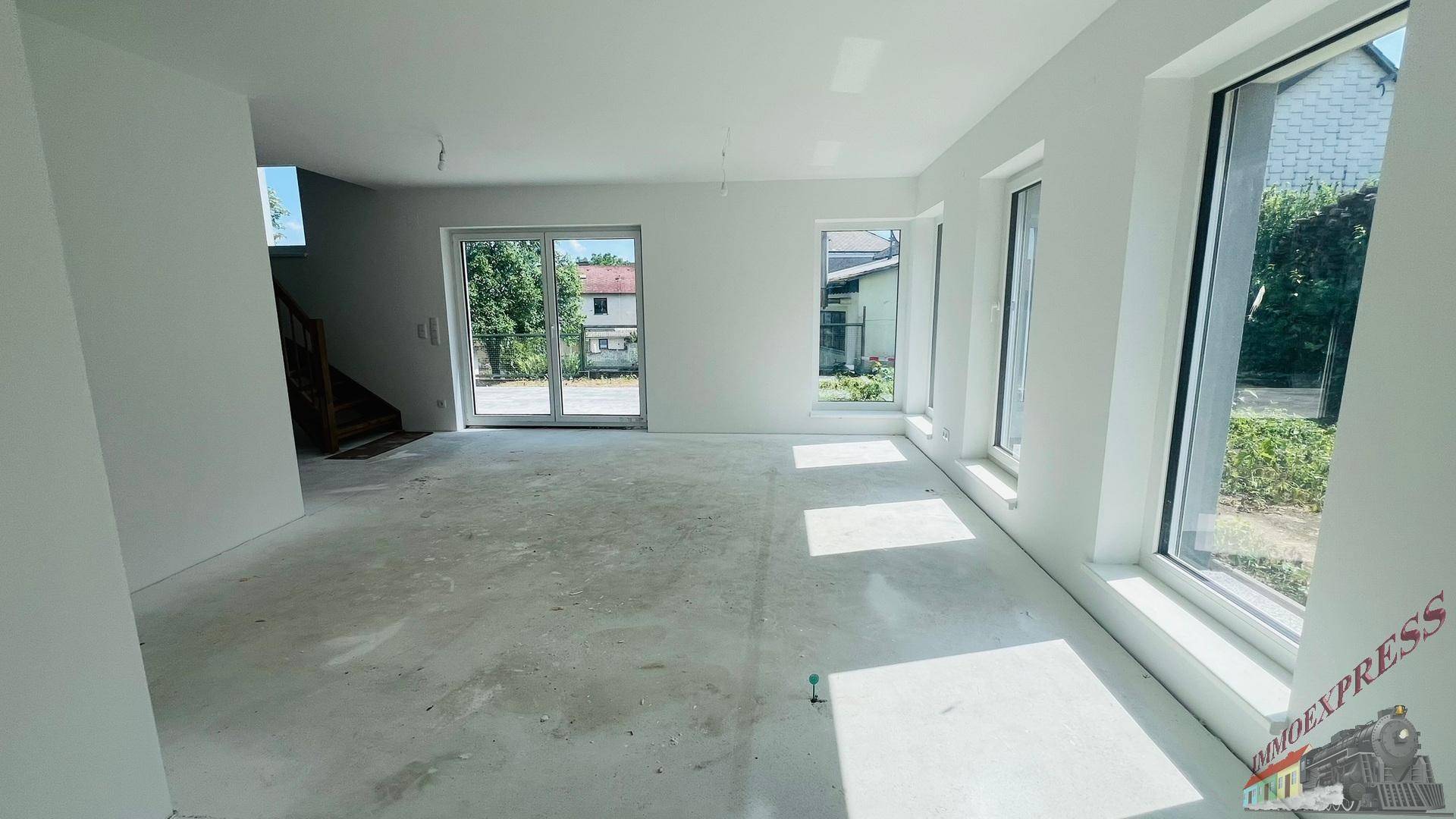 Heller, unmöblierter Wohnraum im Neubau mit großen Fenstern und Zugang zum Außenbereich.