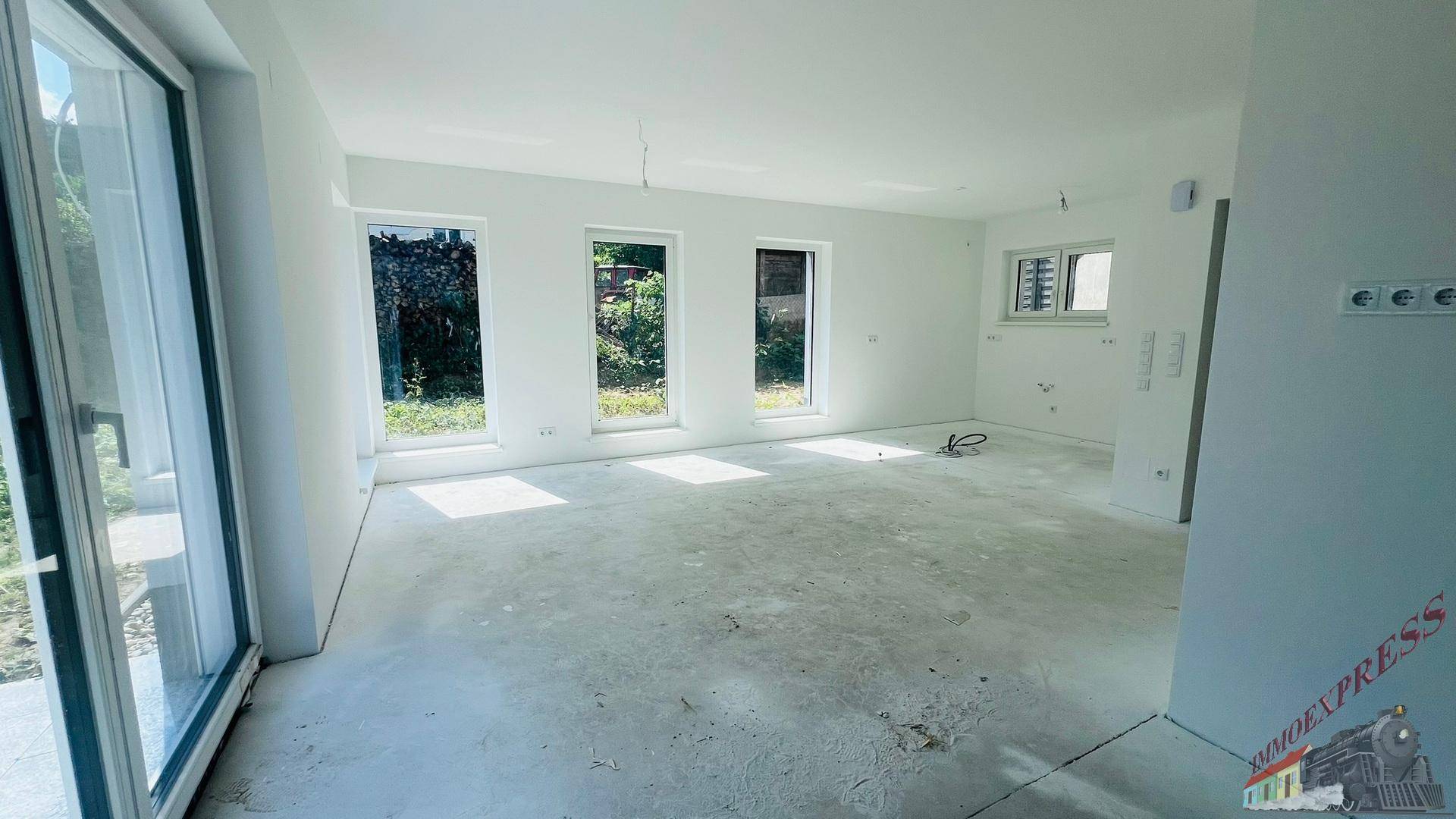 Geräumiger, unmöblierter Wohnraum im Neubau mit großen Fenstern und vorbereiteten Elektroinstallationen.