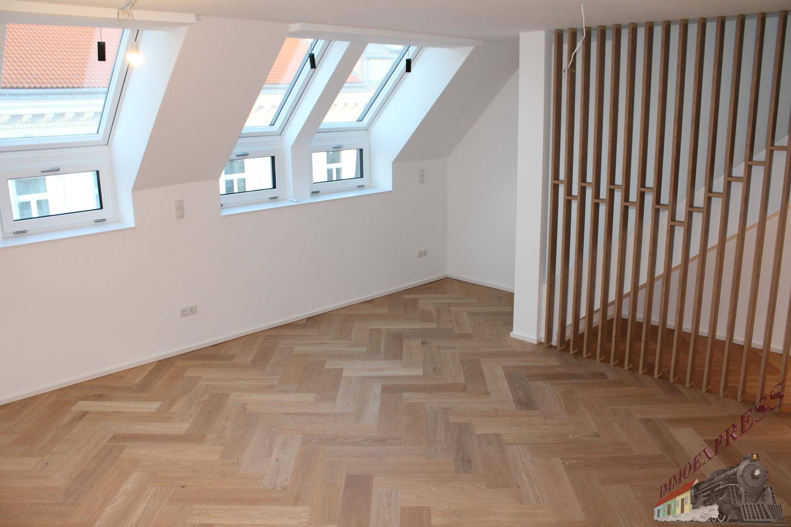Heller Raum im Dachgeschoss mit Fischgrätparkett, Dachfenstern und moderner Holzlamellenwand.