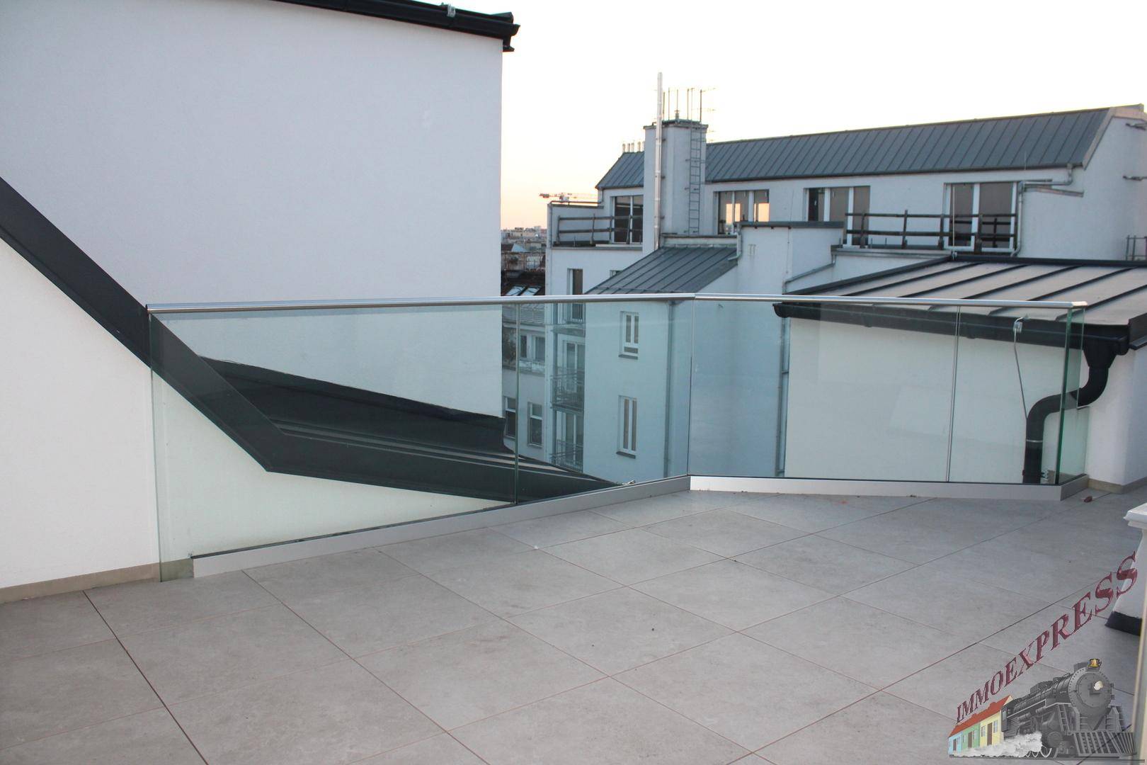 Geräumige Dachterrasse mit modernem Glasgeländer und Blick auf die Dächer der Stadt.
