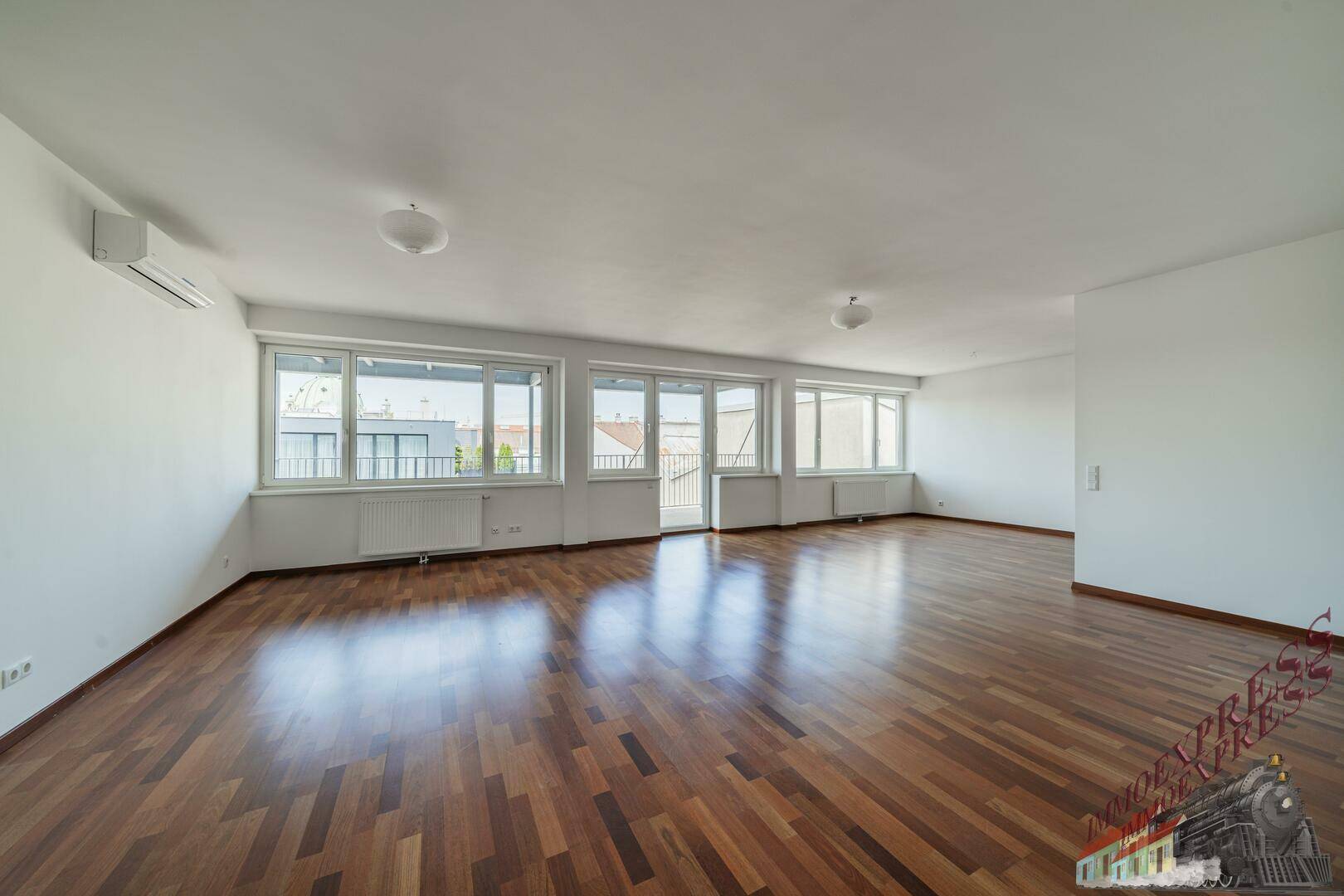 Großzügiges Wohnzimmer mit Parkettboden, Klimaanlage und weitem Blick durch die zahlreichen Fenster.