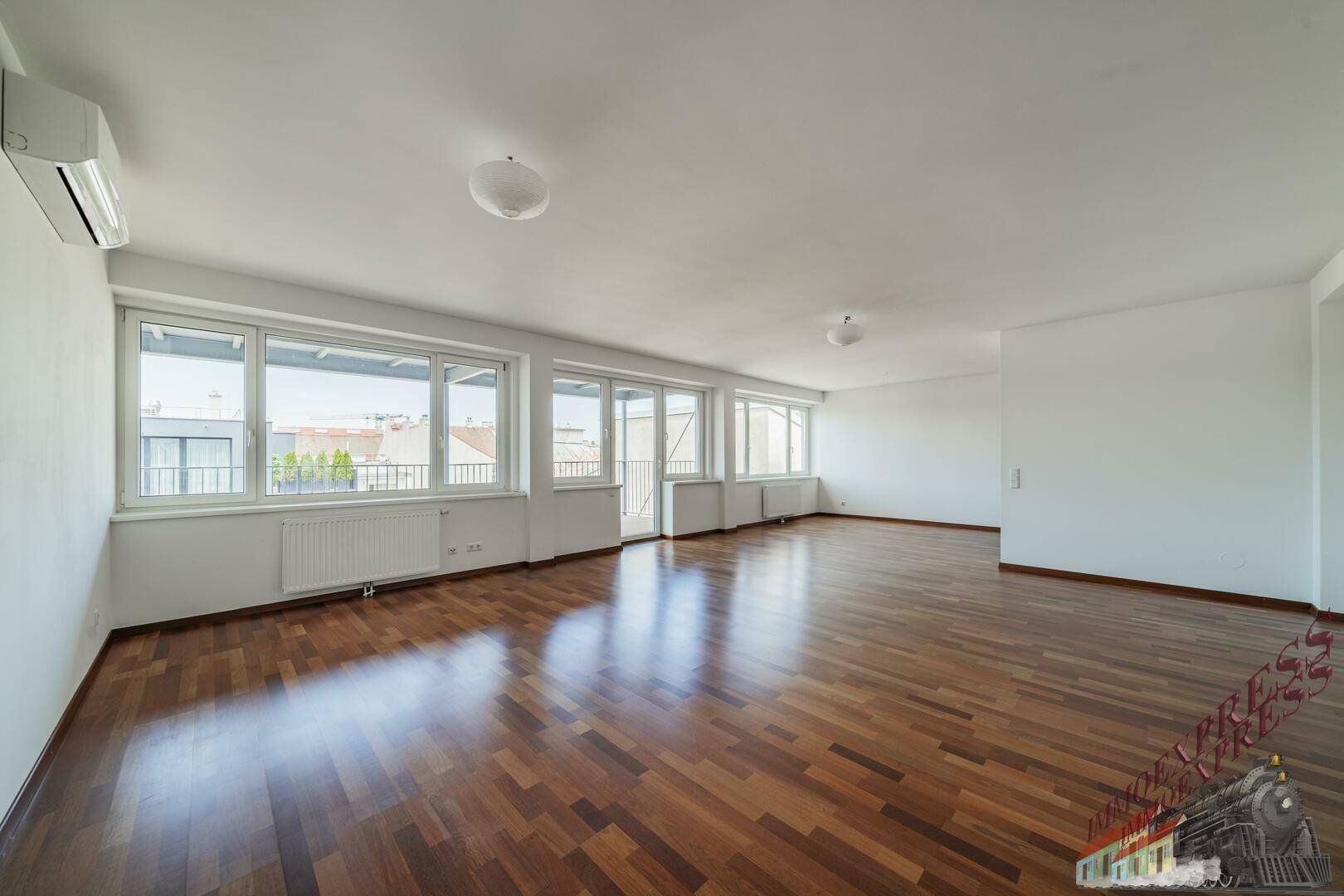 Geräumiges Wohnzimmer mit hellem Parkettboden, Klimaanlage und Zugang zu einem Außenbereich.