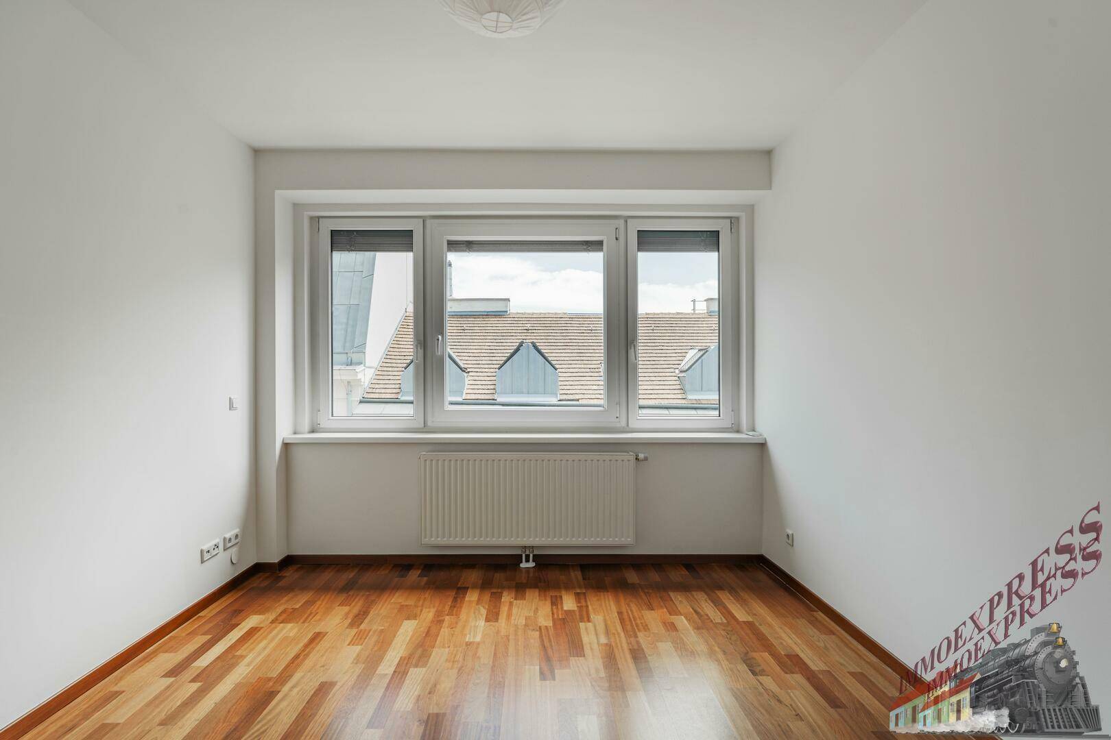 Helles Zimmer mit Parkettboden, großen Fenstern und Blick auf die Dächer.