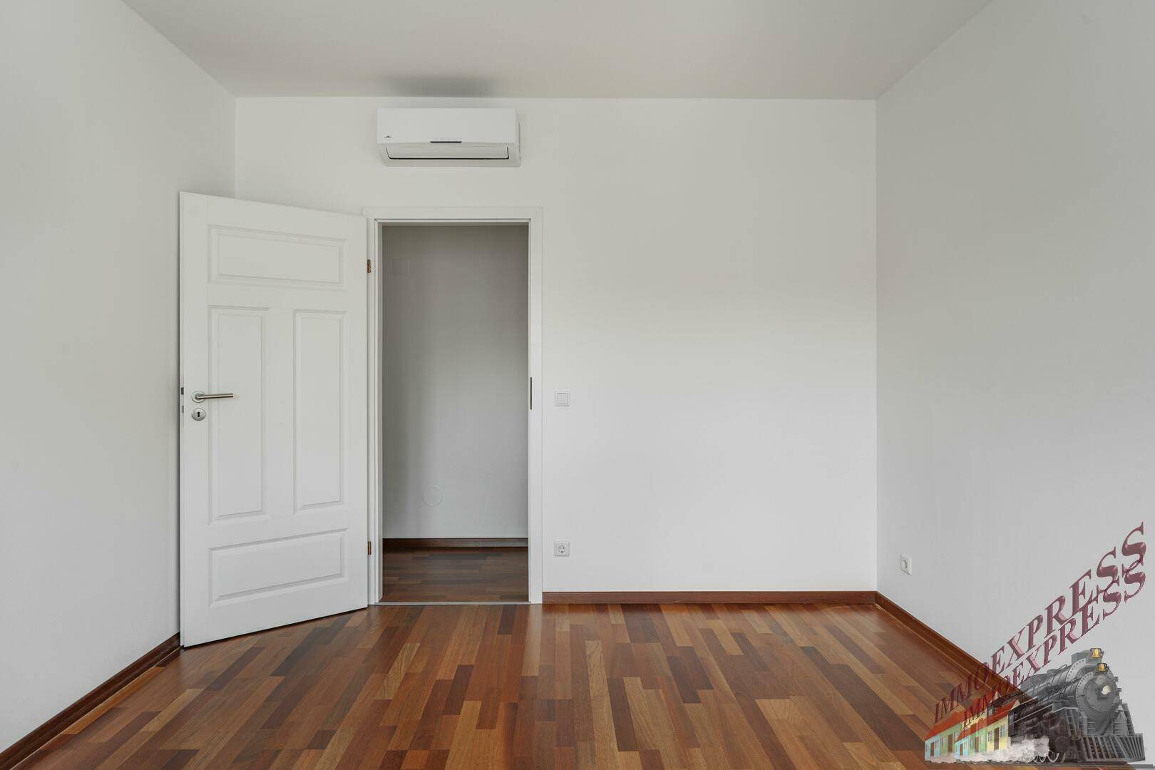 Helles Zimmer mit Parkettboden, weißen Wänden und Klimaanlage.