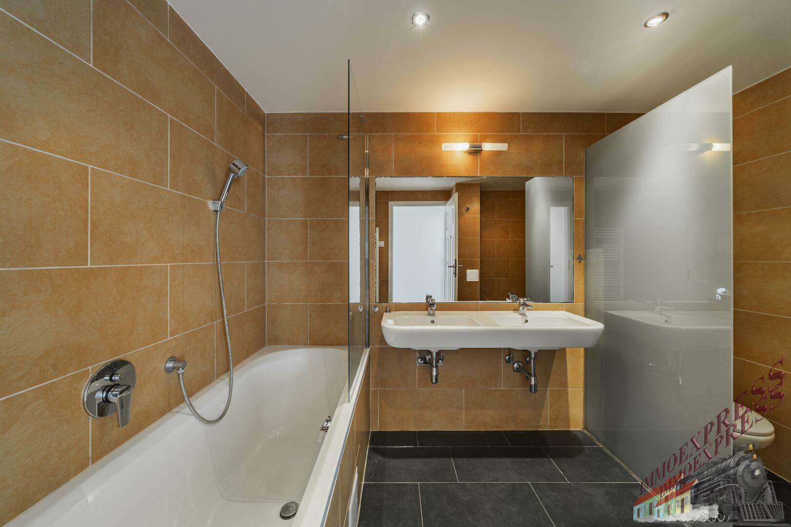 Modernes Badezimmer mit braunen Fliesen, Doppelwaschbecken und Badewanne mit Duschfunktion.