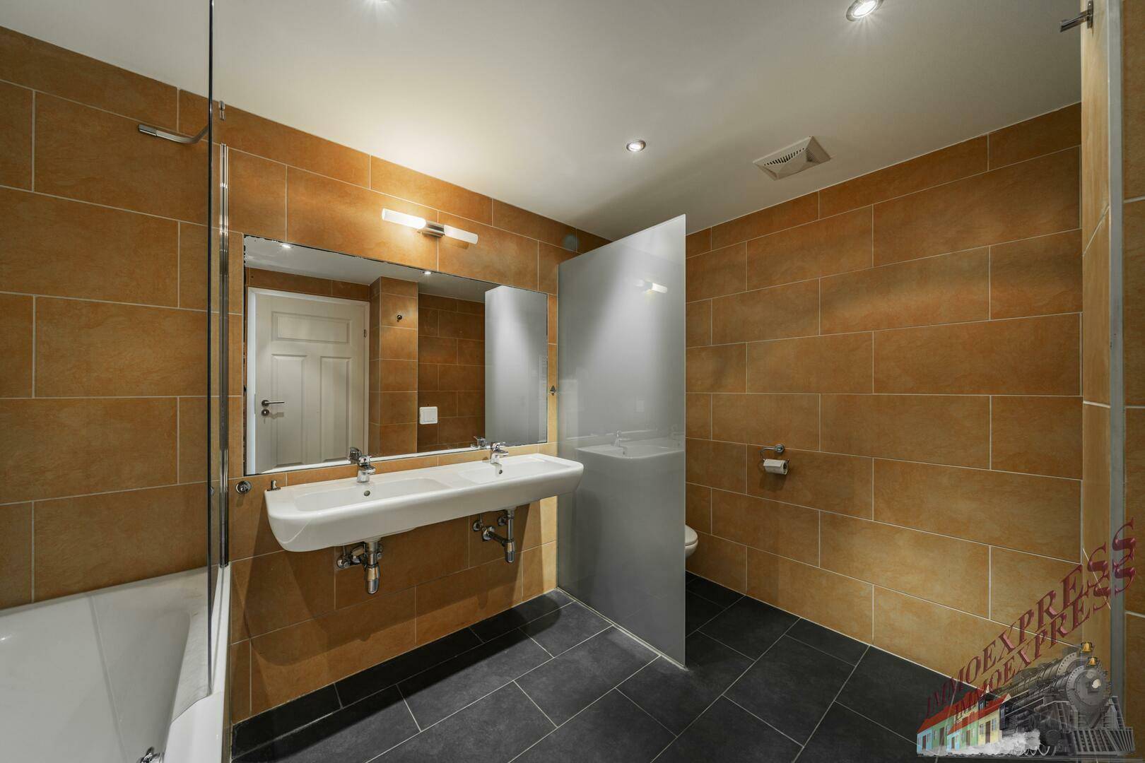 Modernes Badezimmer mit braunen Fliesen, Doppelwaschbecken und Badewanne mit Duschfunktion.