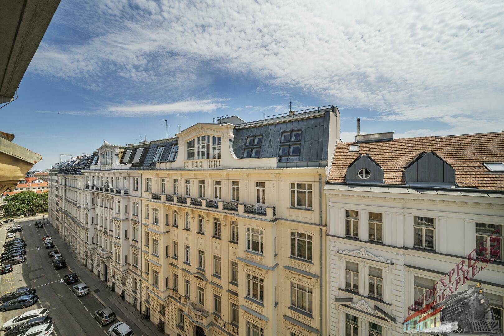 Blick vom Balkon auf eine historische Straße mit charmanten Altbauten und blauem Himmel.