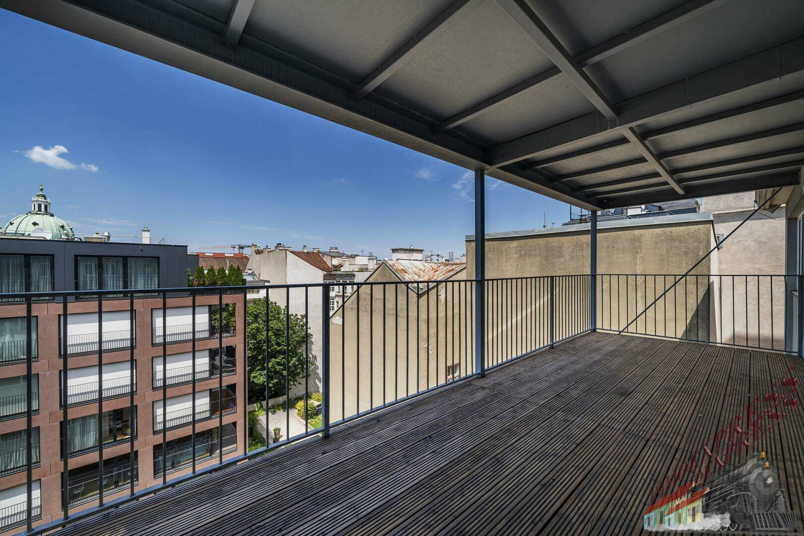 Geräumiger Balkon mit Holzboden und weitem Blick über die Stadt und umliegende Gebäude.