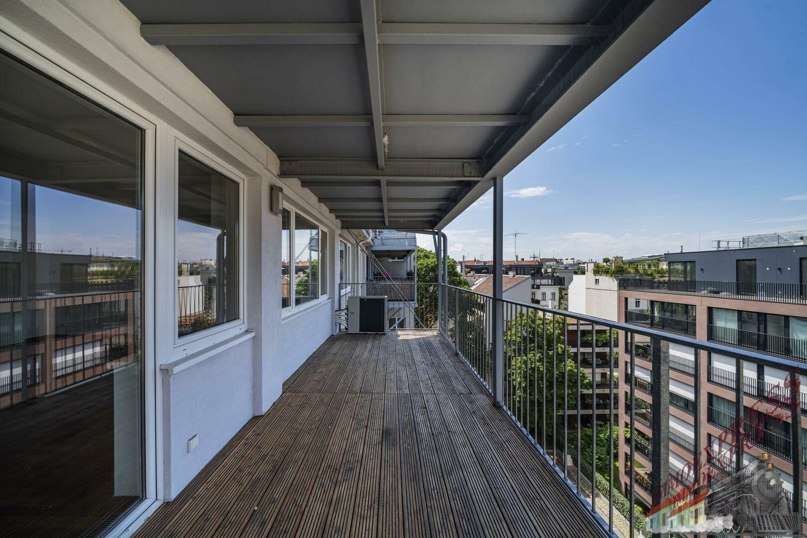 Breiter Balkon mit Holzboden und Blick auf die umliegenden Gebäude und den Himmel.