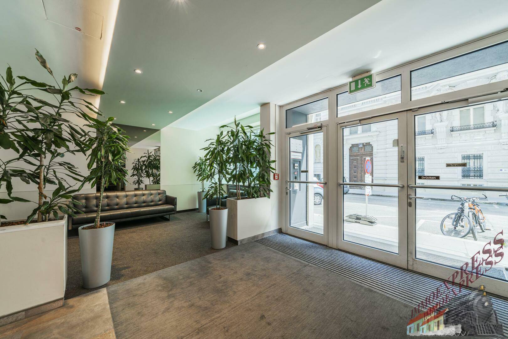 Moderner Eingangsbereich mit großen Glasfronten, Pflanzen und Sitzgelegenheiten.