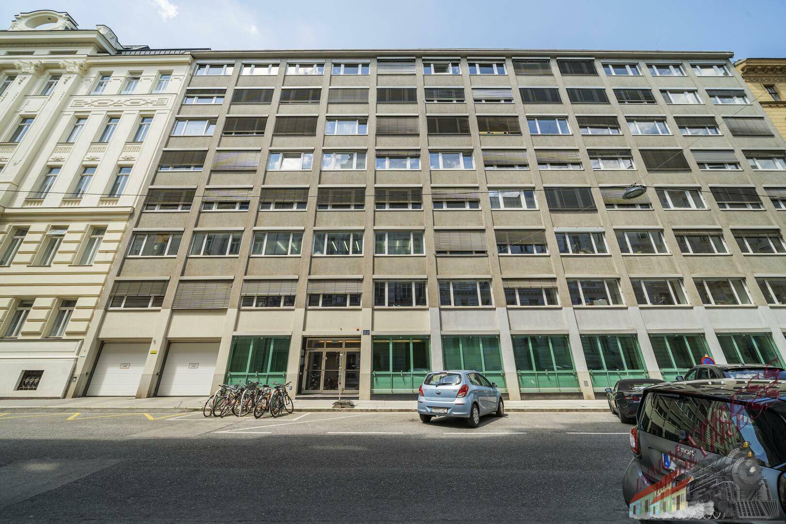 Moderne Fassade eines Gebäudes mit vielen Fenstern und geparkten Autos davor.
