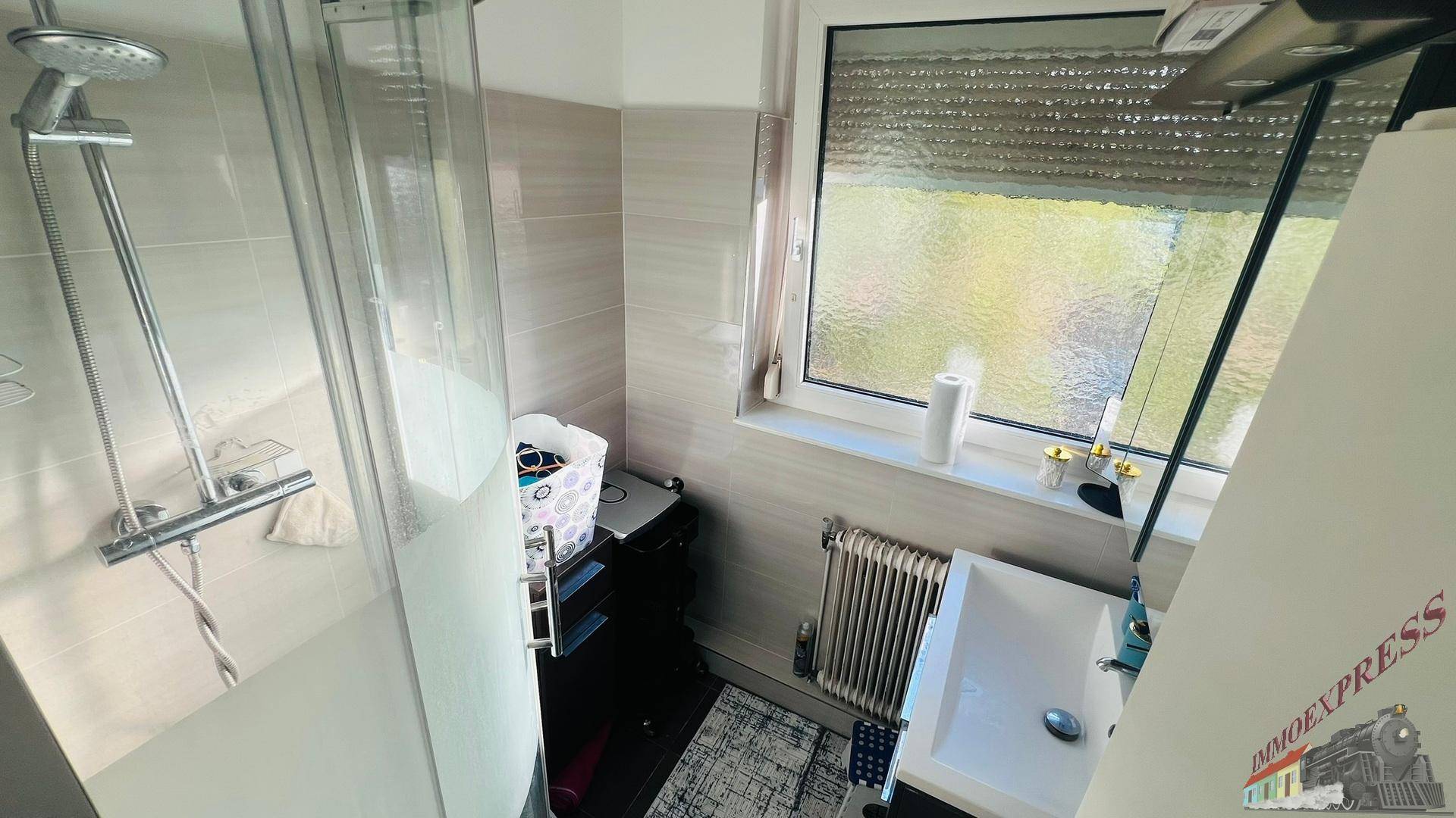 Modernes Badezimmer mit Duschkabine, Waschbecken, Heizkörper und einem Fenster für Tageslicht.