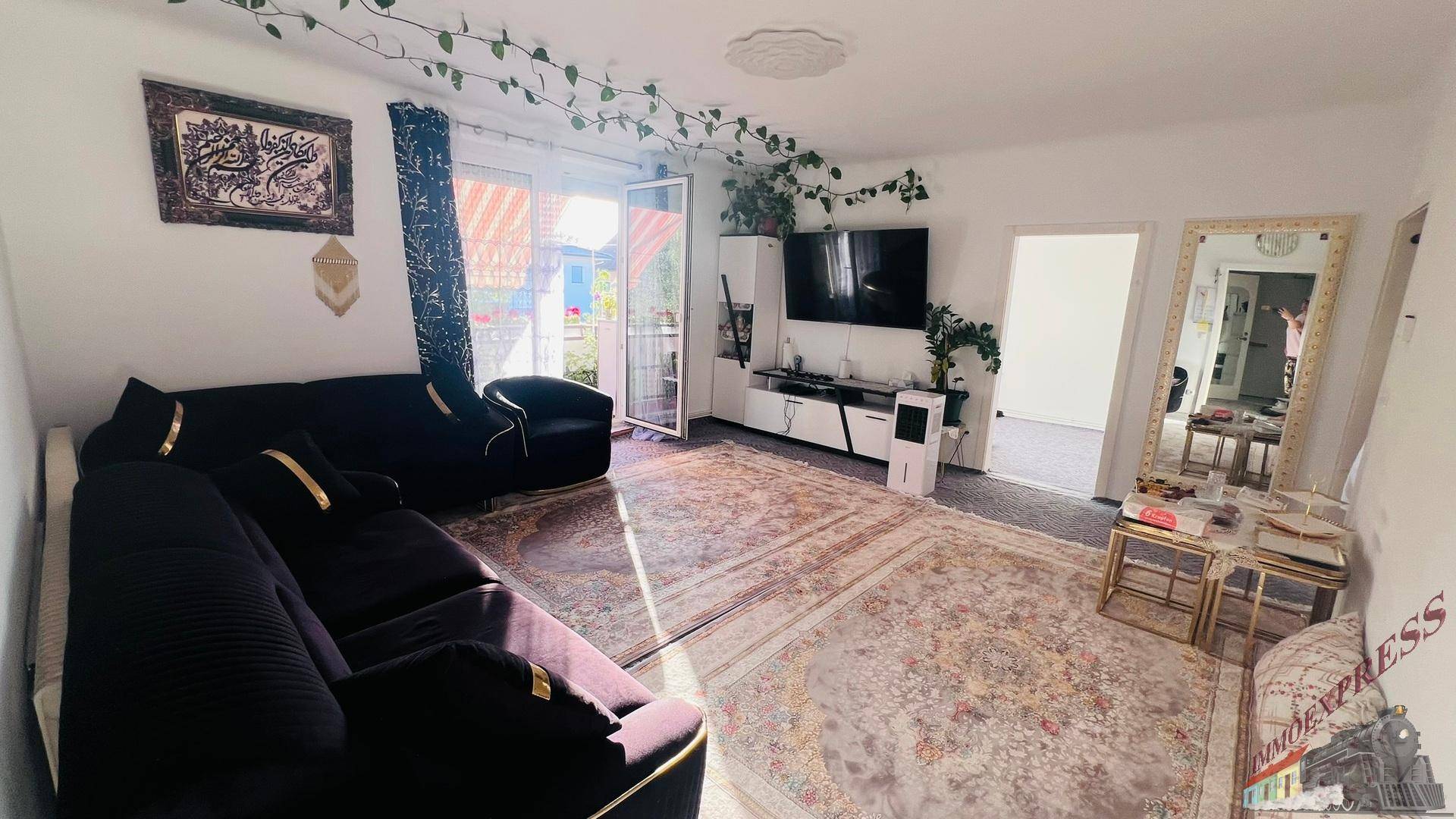 Gemütliches Wohnzimmer mit dunklem Sofa, orientalischem Teppich und Zugang zu einem Außenbereich.