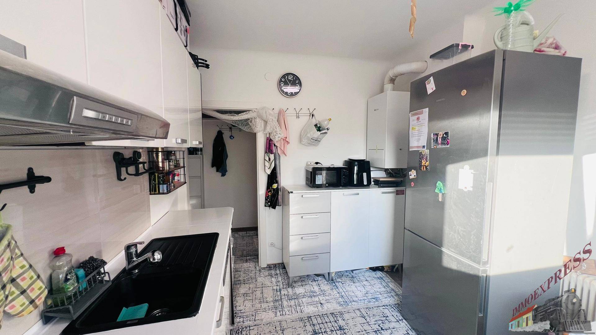 Funktionale Küche mit weißen Schränken, Kühlschrank und Mikrowelle, die zu einem weiteren Raum führt.