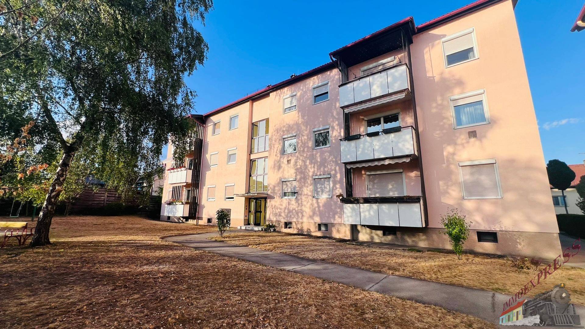 Ansicht des Mehrfamilienhauses mit gepflegtem Vorgarten und Zugangsweg an einem sonnigen Tag.