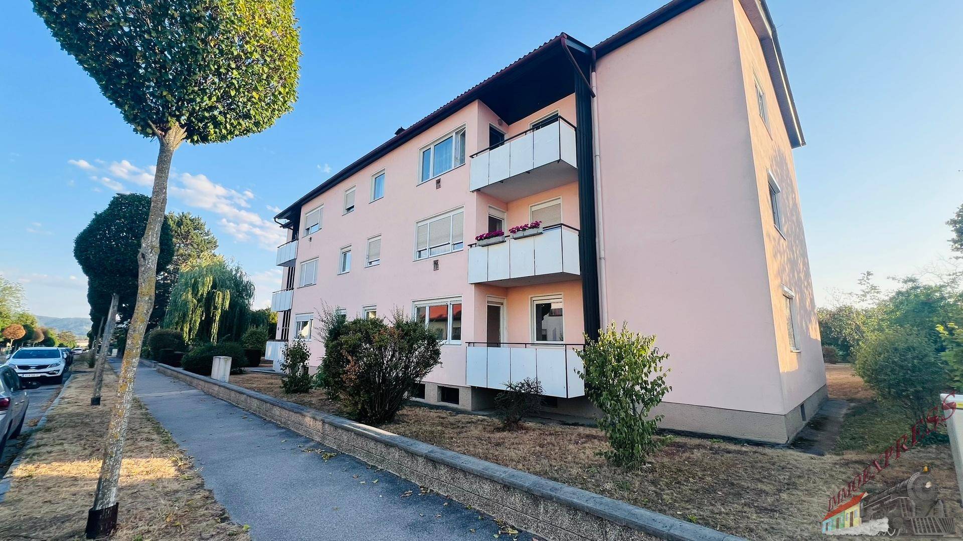 Rosa Mehrfamilienhaus mit mehreren Balkonen und großen Fenstern an einer ruhigen Straße.