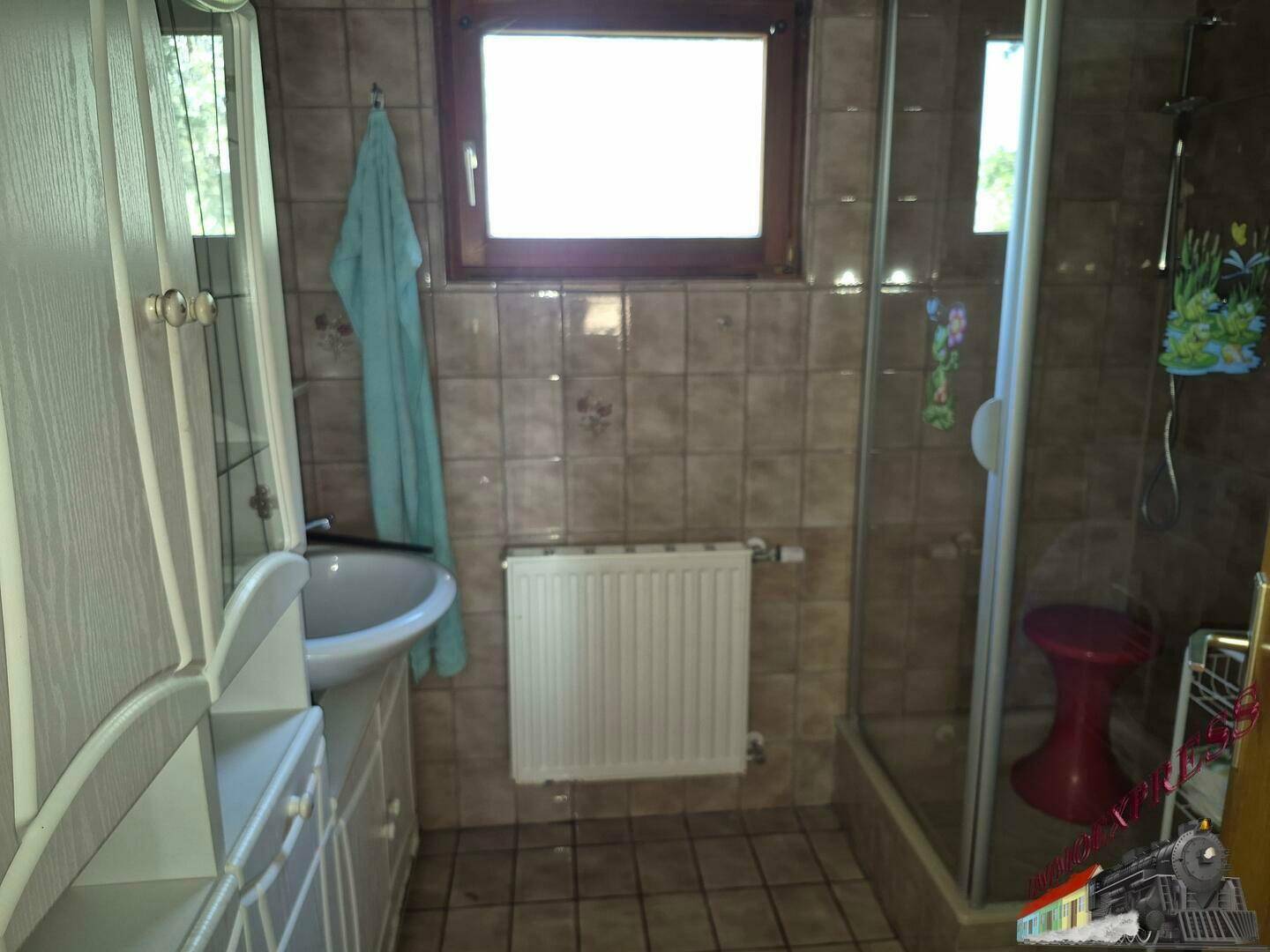 Badezimmer mit braunen Fliesen, Waschbecken, Heizkörper und Duschkabine.