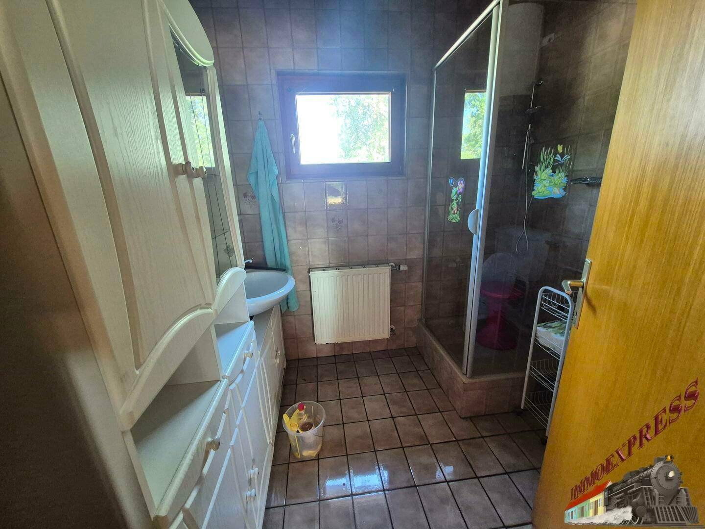 Gefliestes Badezimmer mit Duschkabine, Waschbecken und Fenster für Tageslicht.