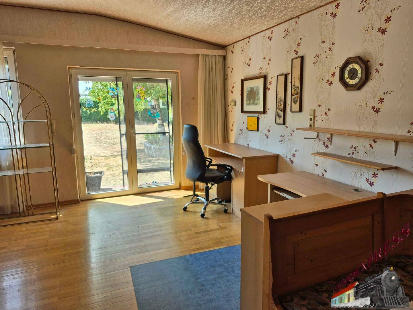 Helles Arbeitszimmer mit Schreibtisch, floraler Tapete und direktem Zugang zum Garten.