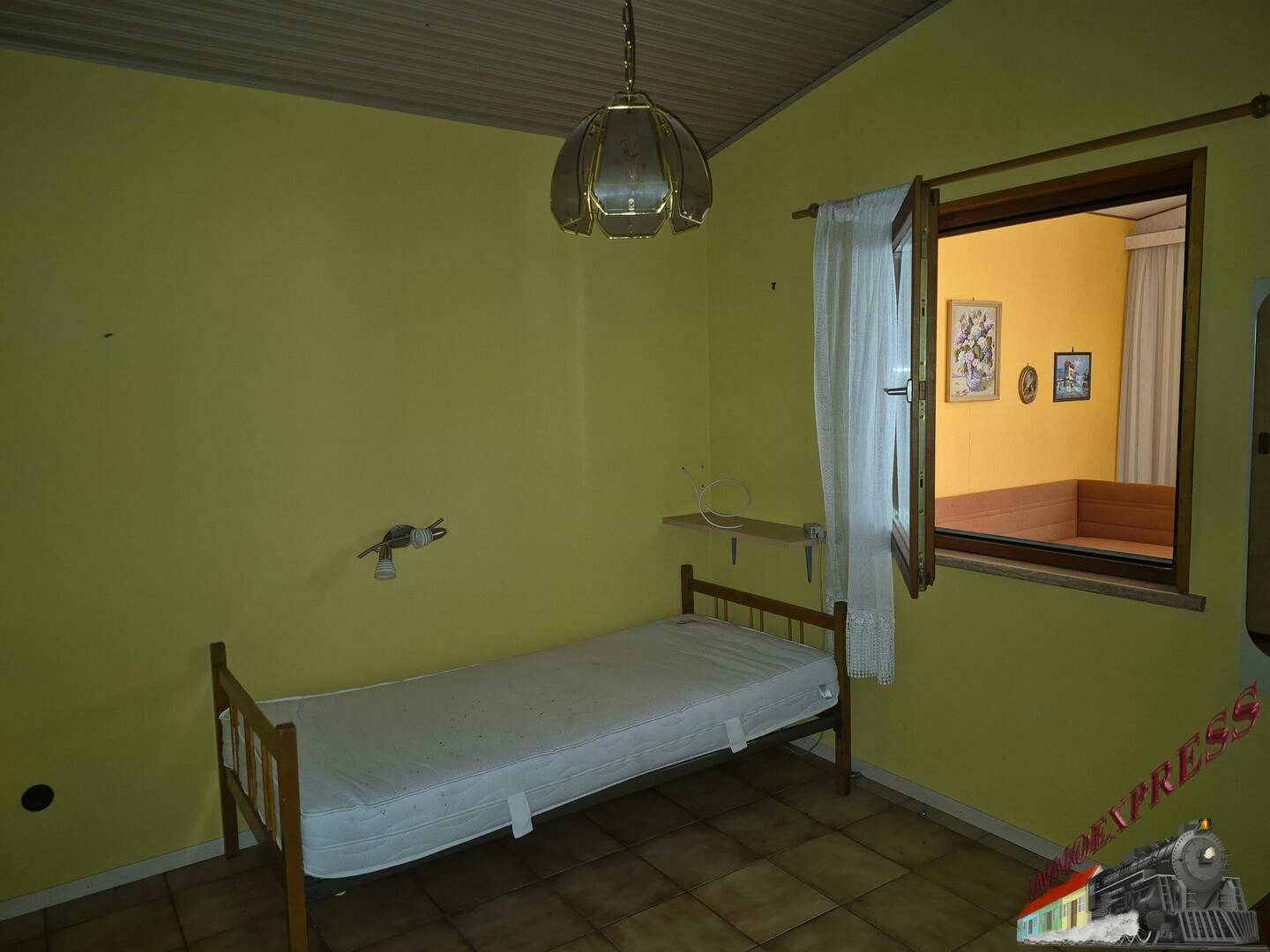 Schlafzimmer mit Einzelbett, gelben Wänden und Fenster mit Blick in den Nebenraum.