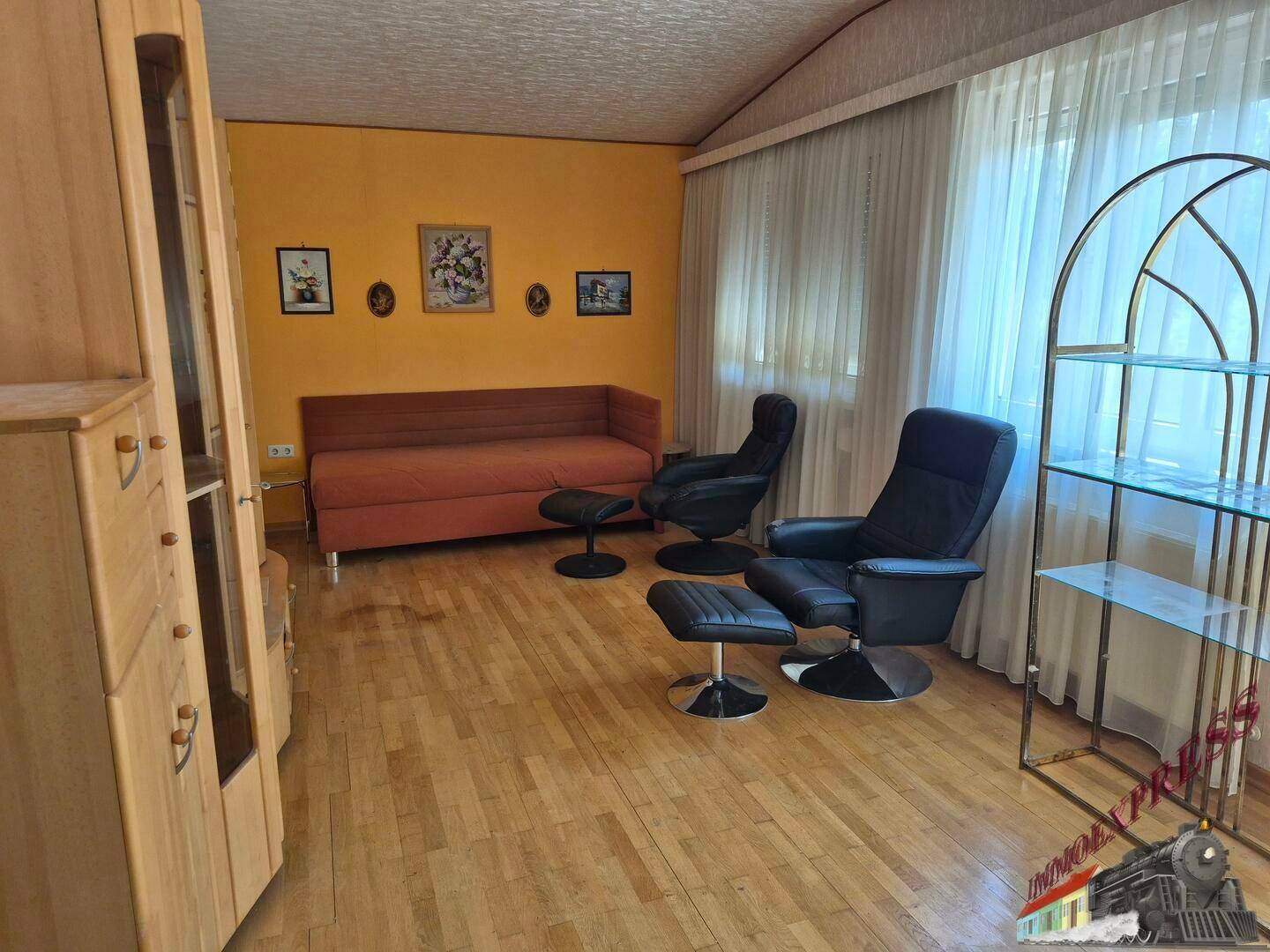Wohnzimmer mit Holzfußboden, bequemen Sesseln, Sofa und Vitrinenschrank.