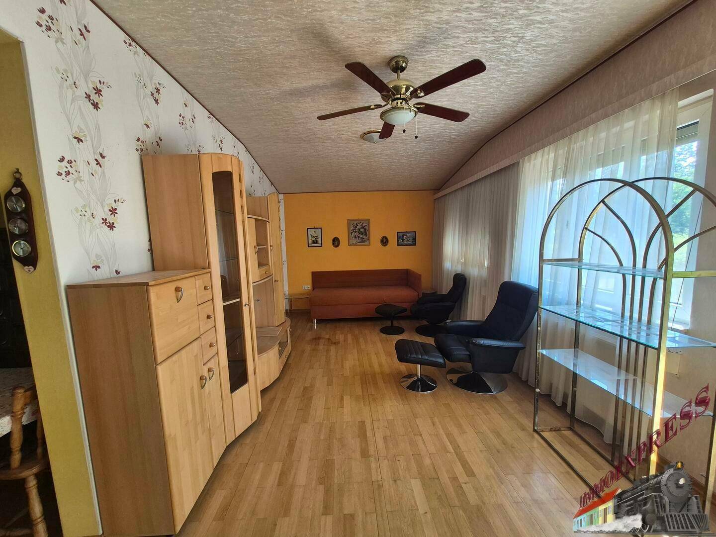 Geräumiges Wohnzimmer mit Holzfußboden, Deckenventilator und viel Tageslicht.