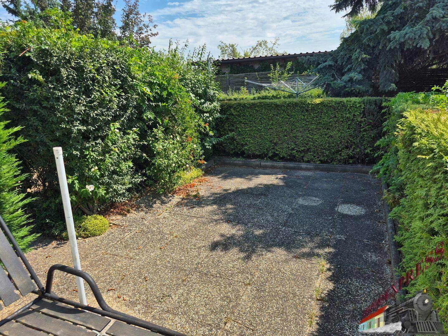 Gepflasterter Außenbereich umgeben von hohen Hecken und Bäumen, ideal als Stellplatz.