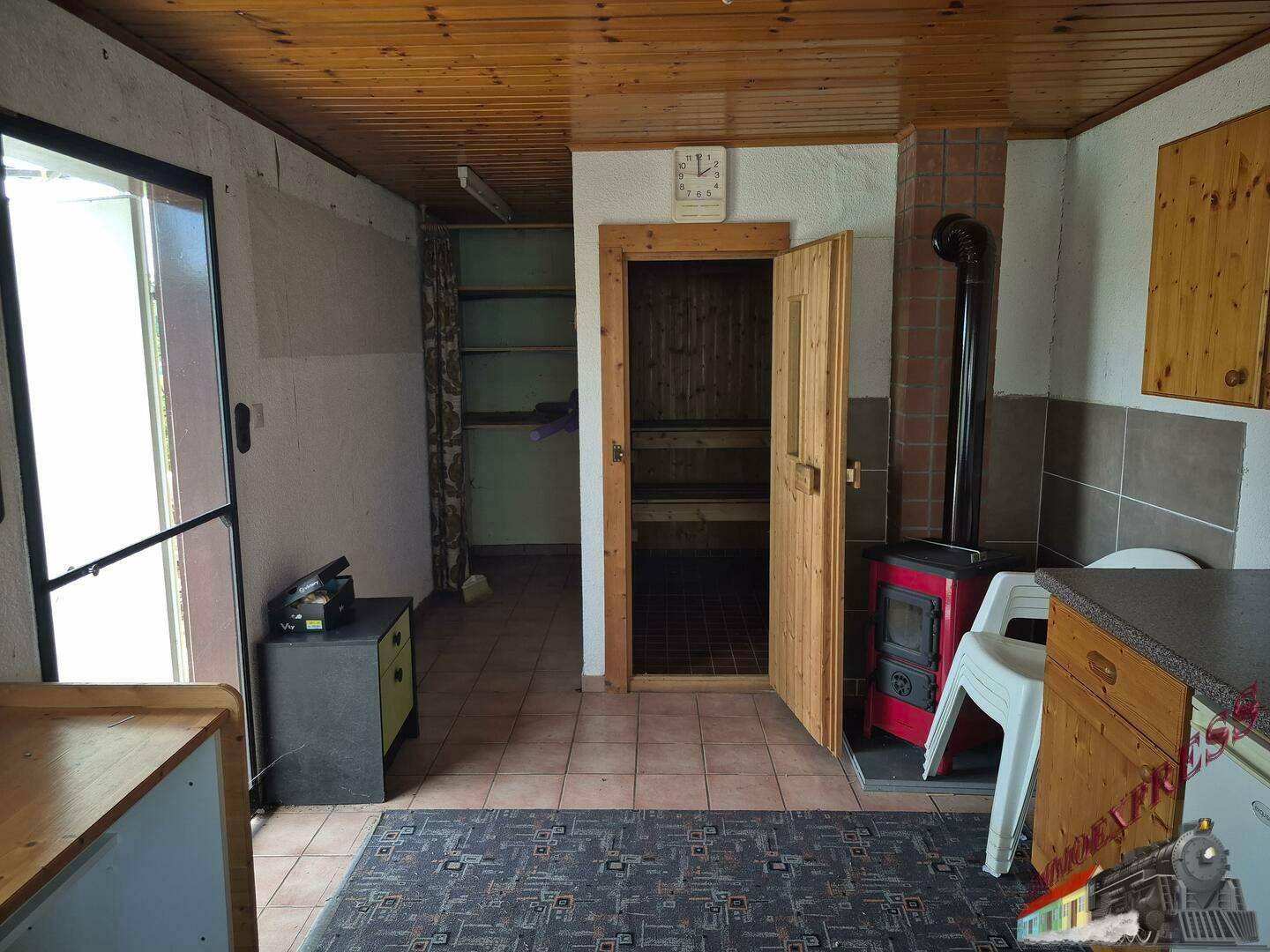 Flur- oder Hauswirtschaftsbereich mit Zugang zur Sauna und einem Holzofen, gefliestem Boden.