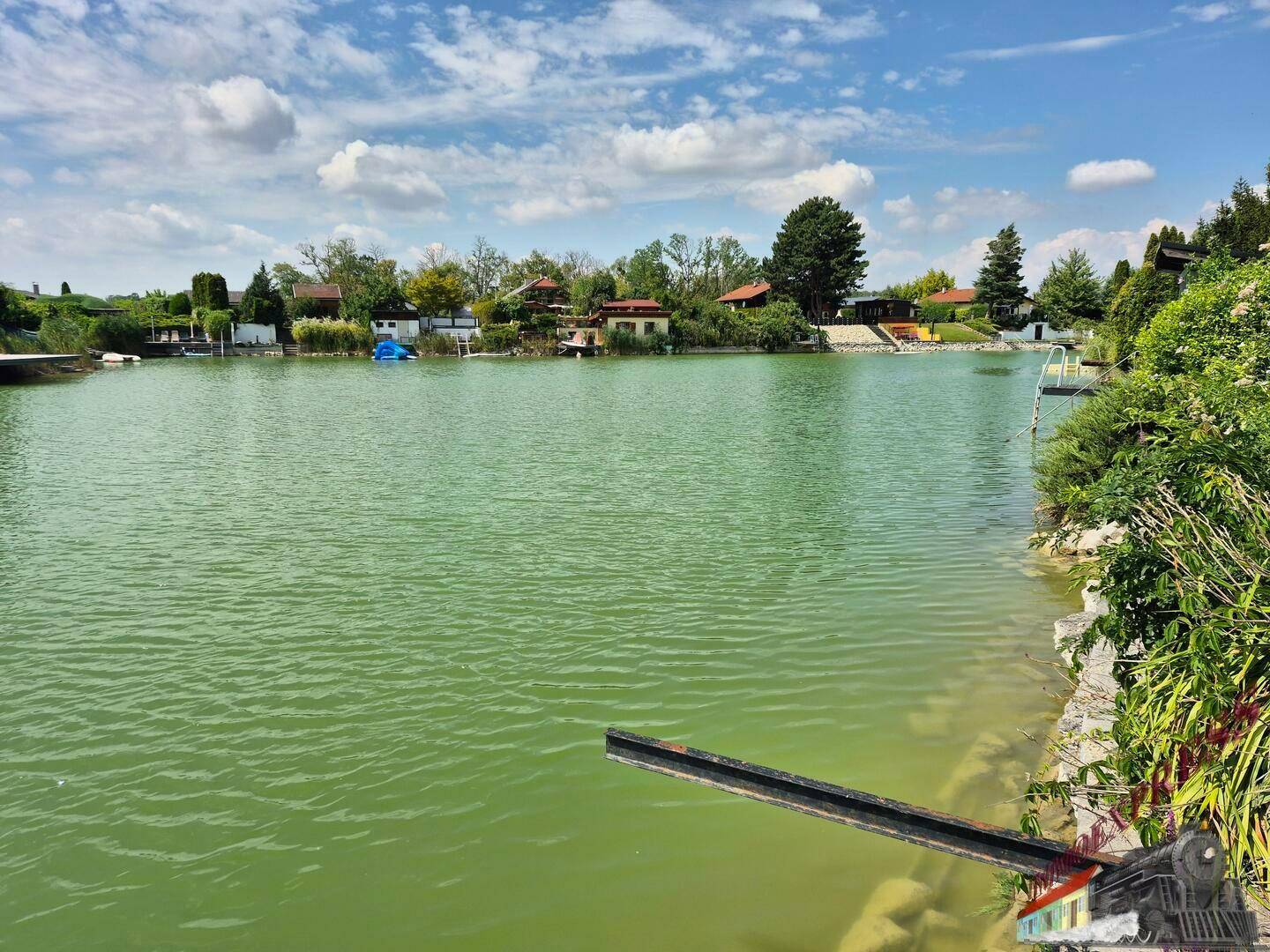 Malerischer Blick auf einen See mit Häusern am gegenüberliegenden Ufer unter blauem Himmel.
