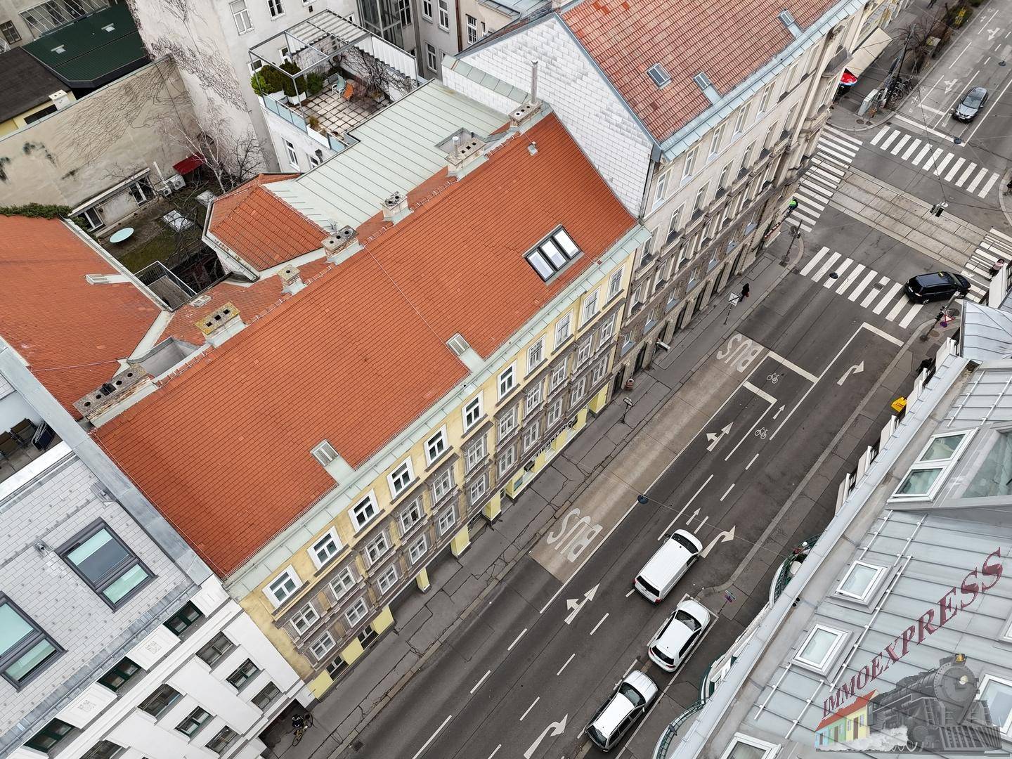 Luftaufnahme eines Wohngebäudes mit rotem Dach und belebter Straße in der Stadt.