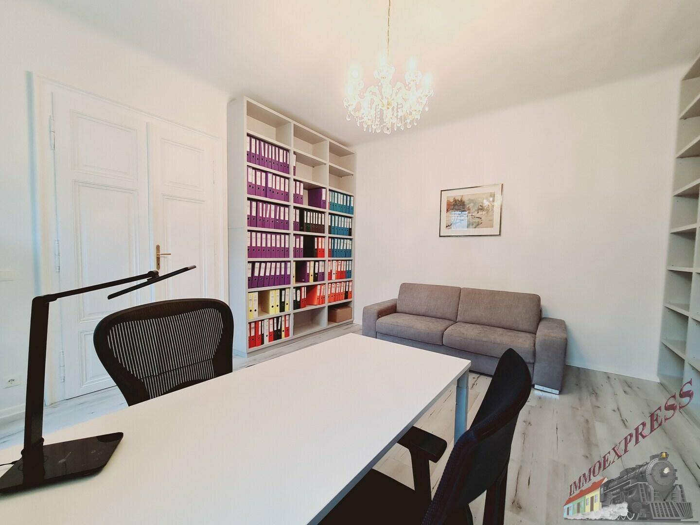 Geräumiges Büro mit großem Schreibtisch, Bücherregalen und bequemer Sitzgelegenheit.